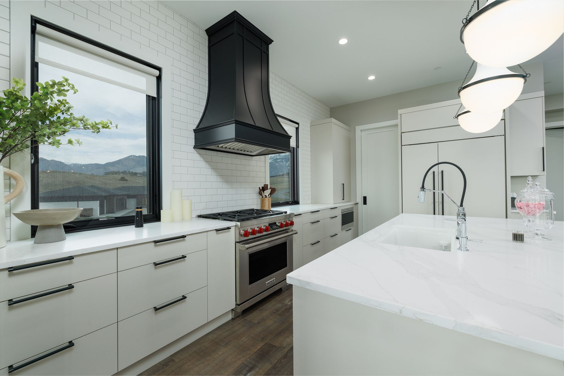 Modern white kitchen with black range hood, marble island, and large window overlooking mountains
