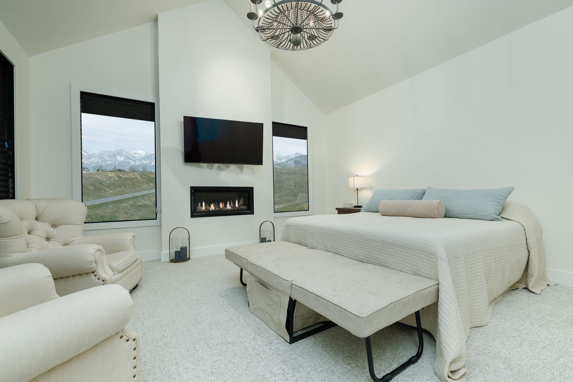 Bright modern bedroom with a bed, bench, wall-mounted TV, fireplace, and large windows