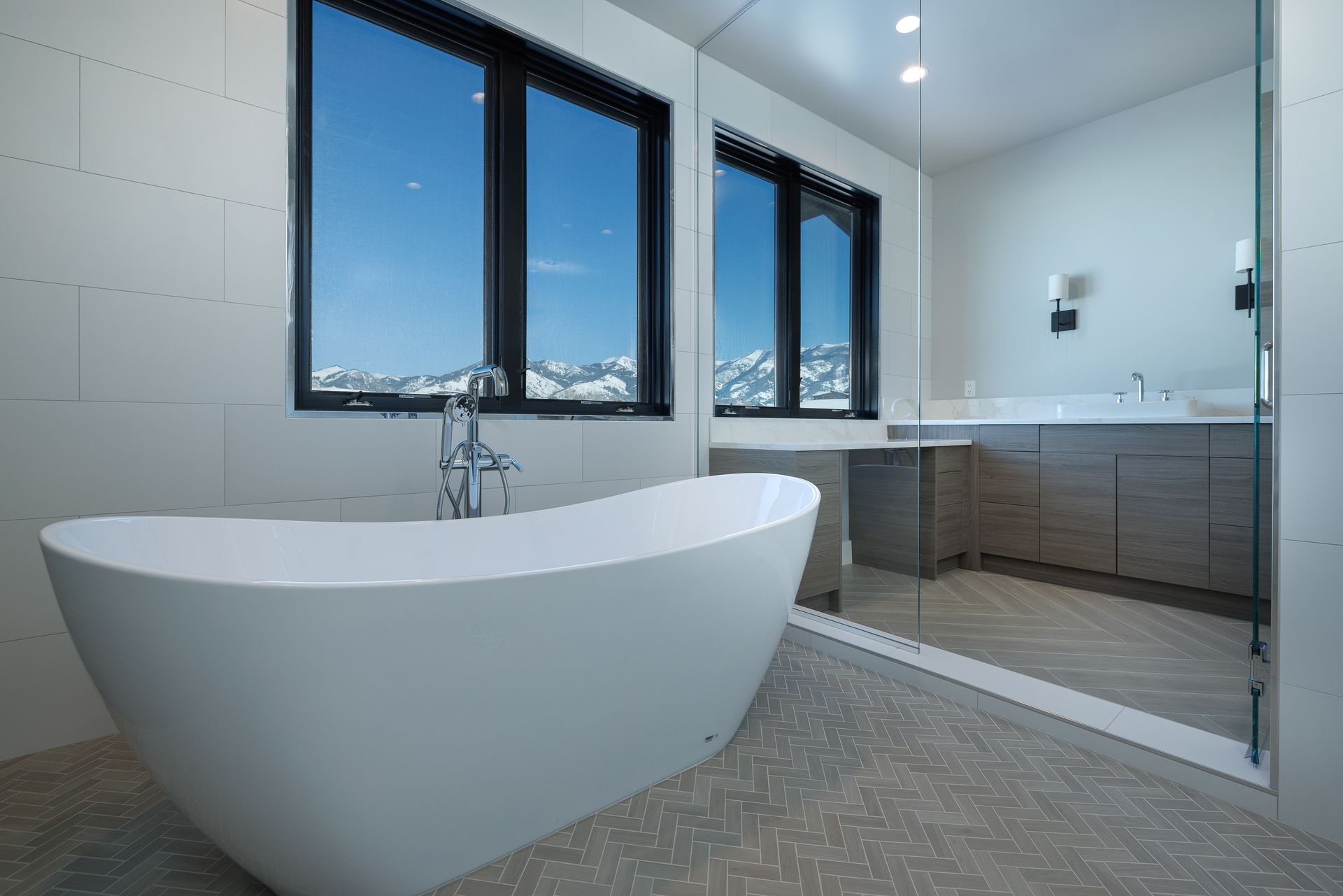 Modern bathroom with a freestanding white tub, double windows, and a glass-enclosed shower.