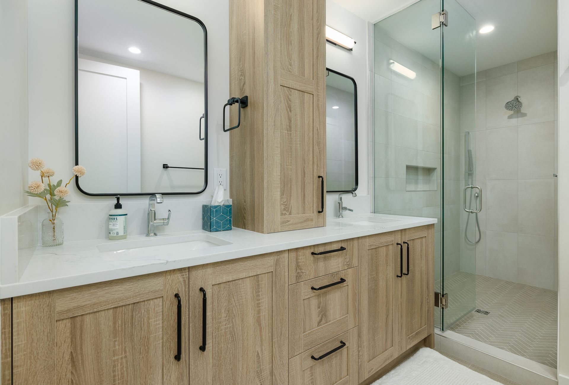Modern bathroom vanity with wood cabinets, double mirrors, and glass shower enclosure