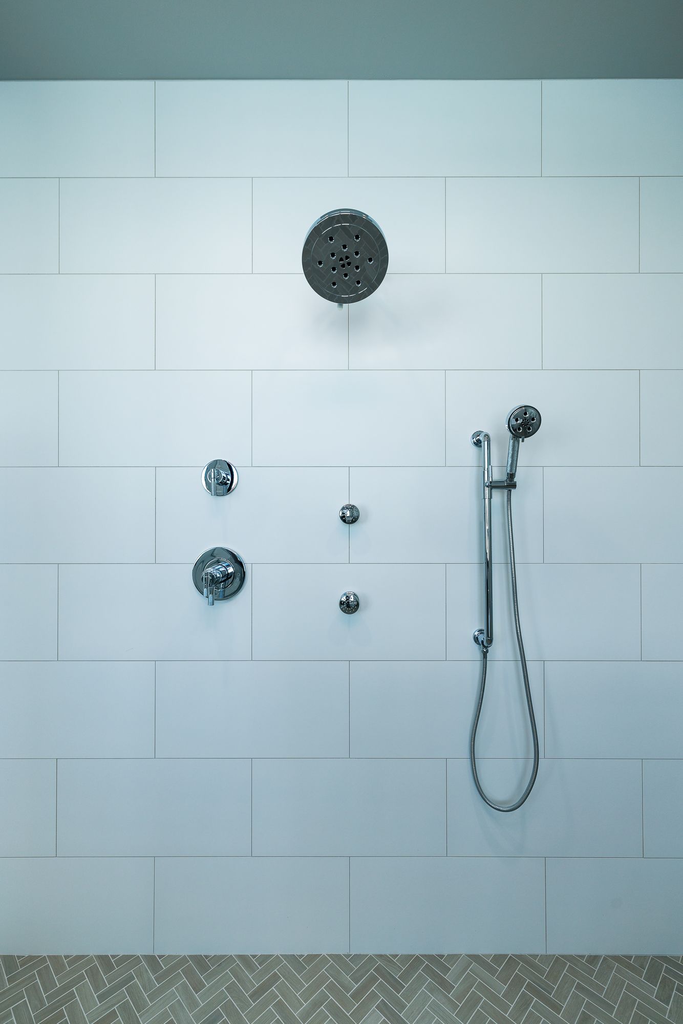 Modern tiled shower with rainfall head, handheld sprayer, and control knobs.