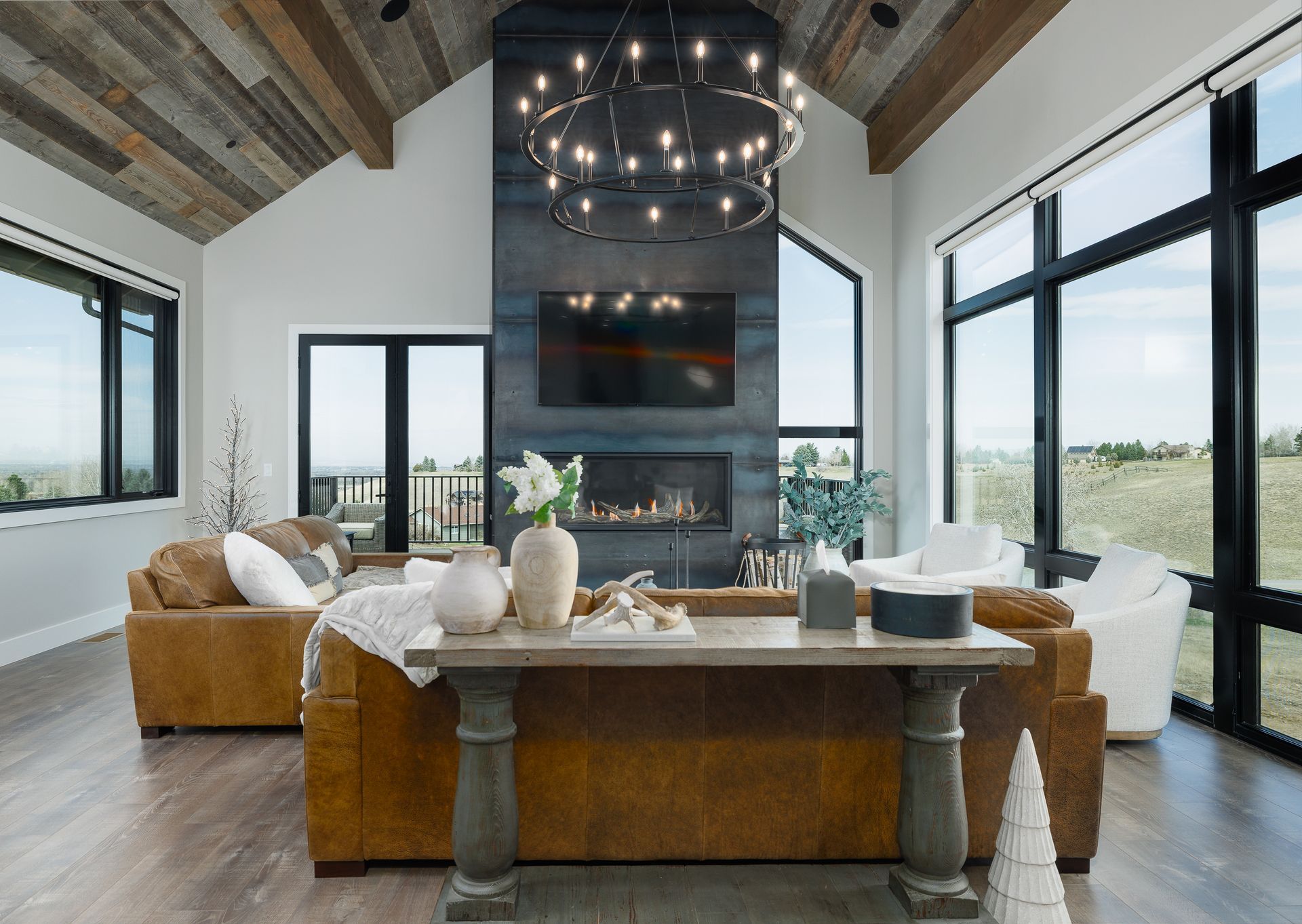 Modern living room with vaulted ceiling, fireplace, large windows, and neutral-toned seating around a wooden coffee table