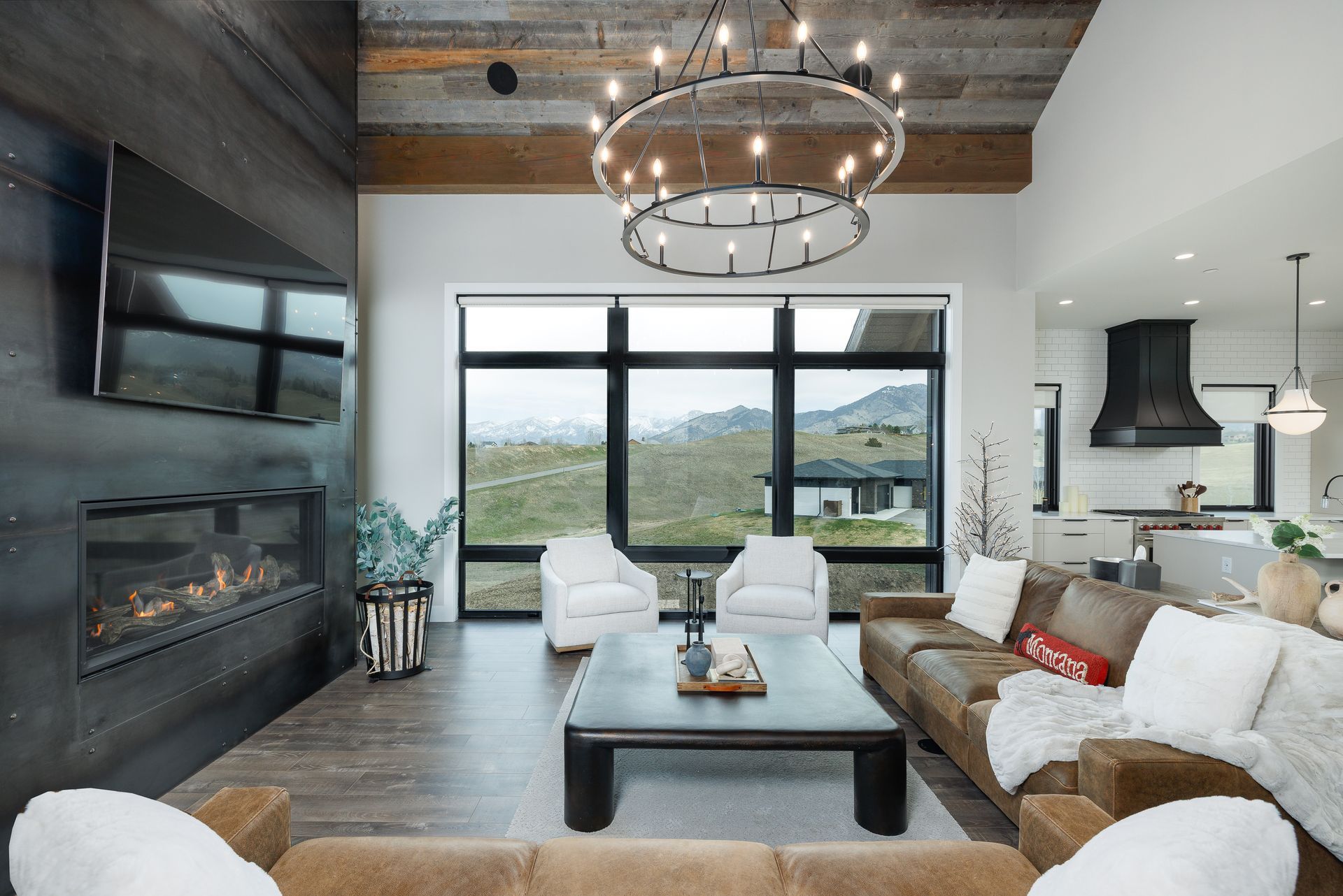 Modern living room with fireplace, large window, white seating, and rustic chandelier