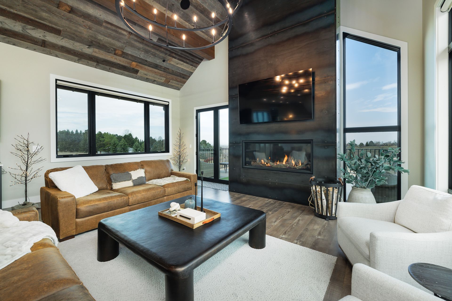 Modern living room with high wood ceiling, large windows, fireplace, wicker sofa, and black coffee table