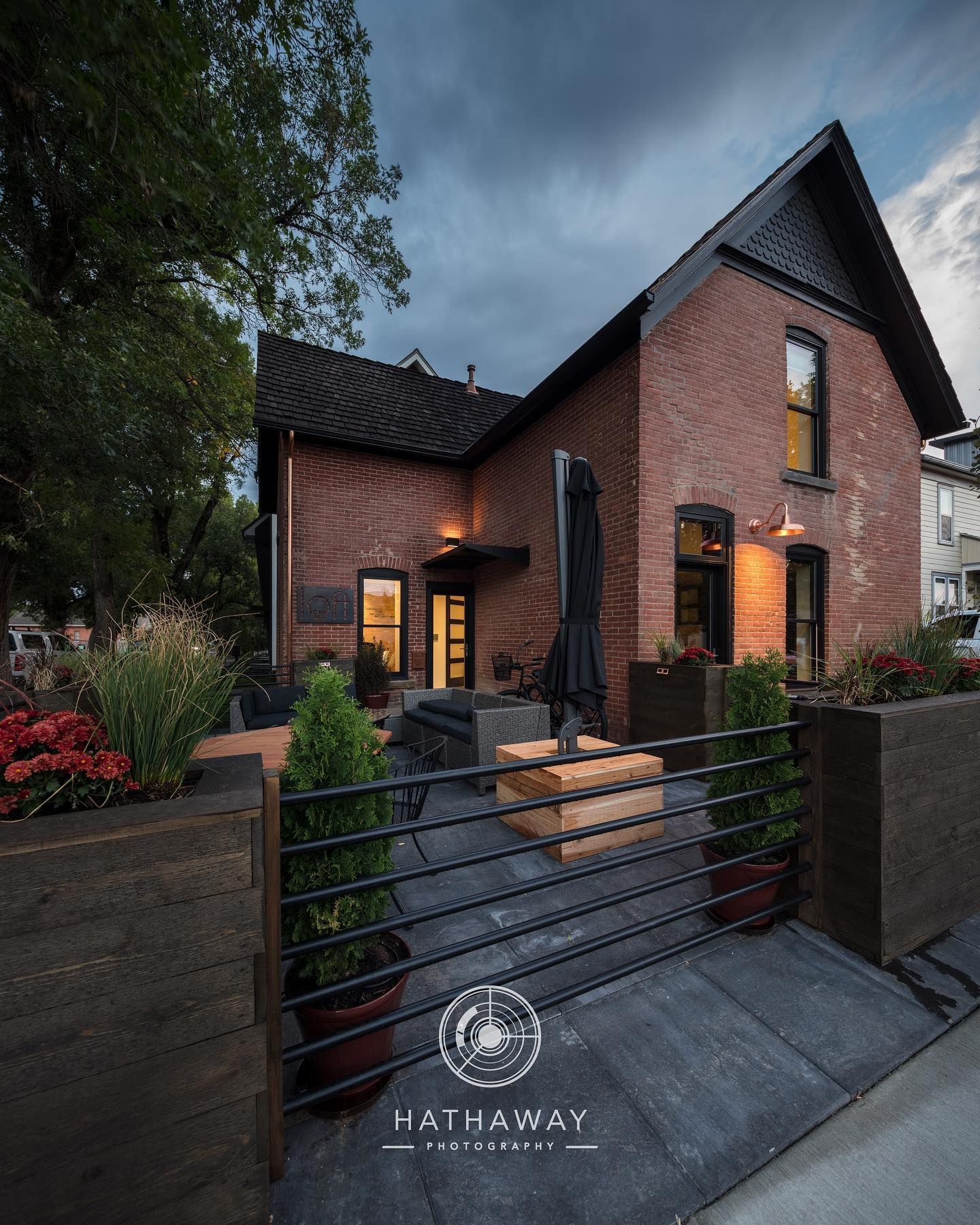 A red brick home at dusk with a dark metal fence, tiered outdoor seating, and warm exterior lighting.
