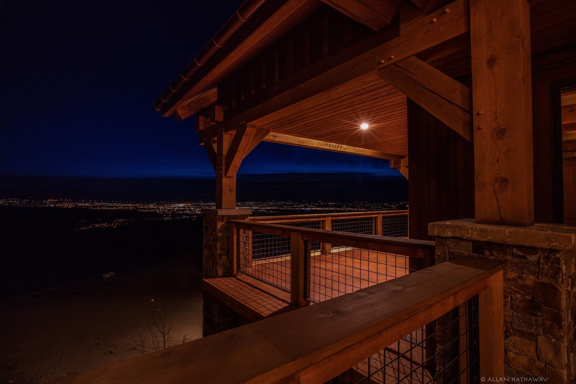 A wooden deck at night, overlooking a glowing city skyline under a dark blue twilight sky.