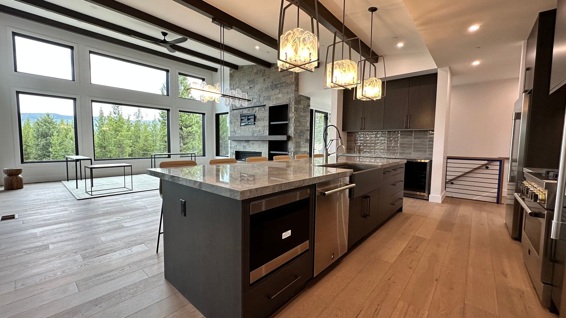 A modern kitchen island with dark cabinetry and granite countertops, opening into a bright living space with large windows.