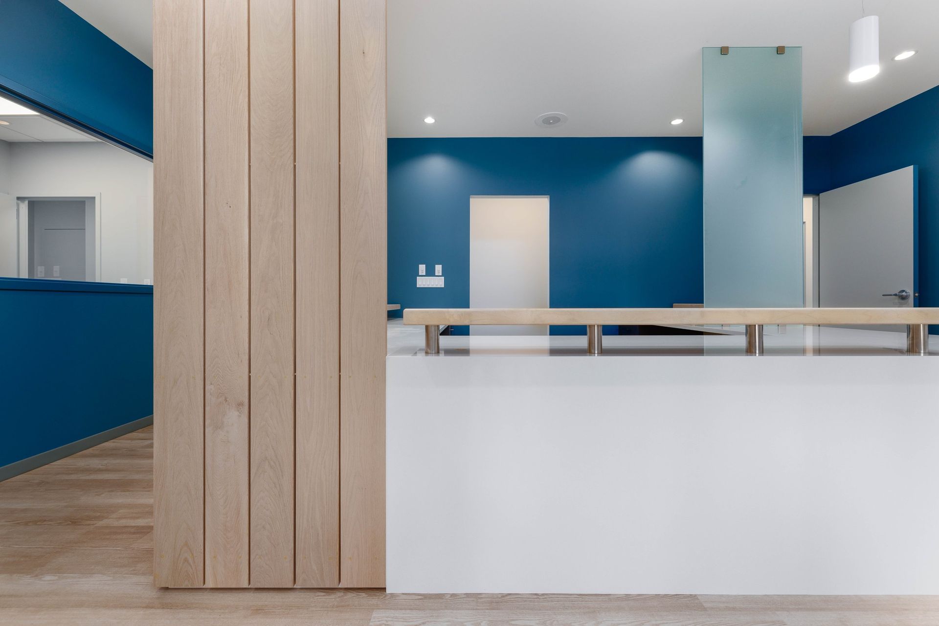 A reception desk with a white front and wood slat column, set against a blue wall in a modern, brightly lit office space.