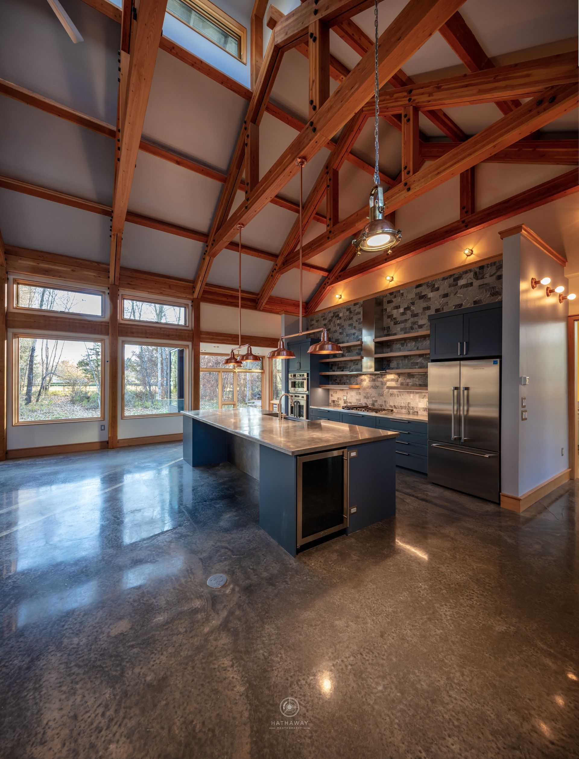 Modern kitchen with vaulted wood-beamed ceilings, polished concrete floors, blue island, and stainless steel appliances.