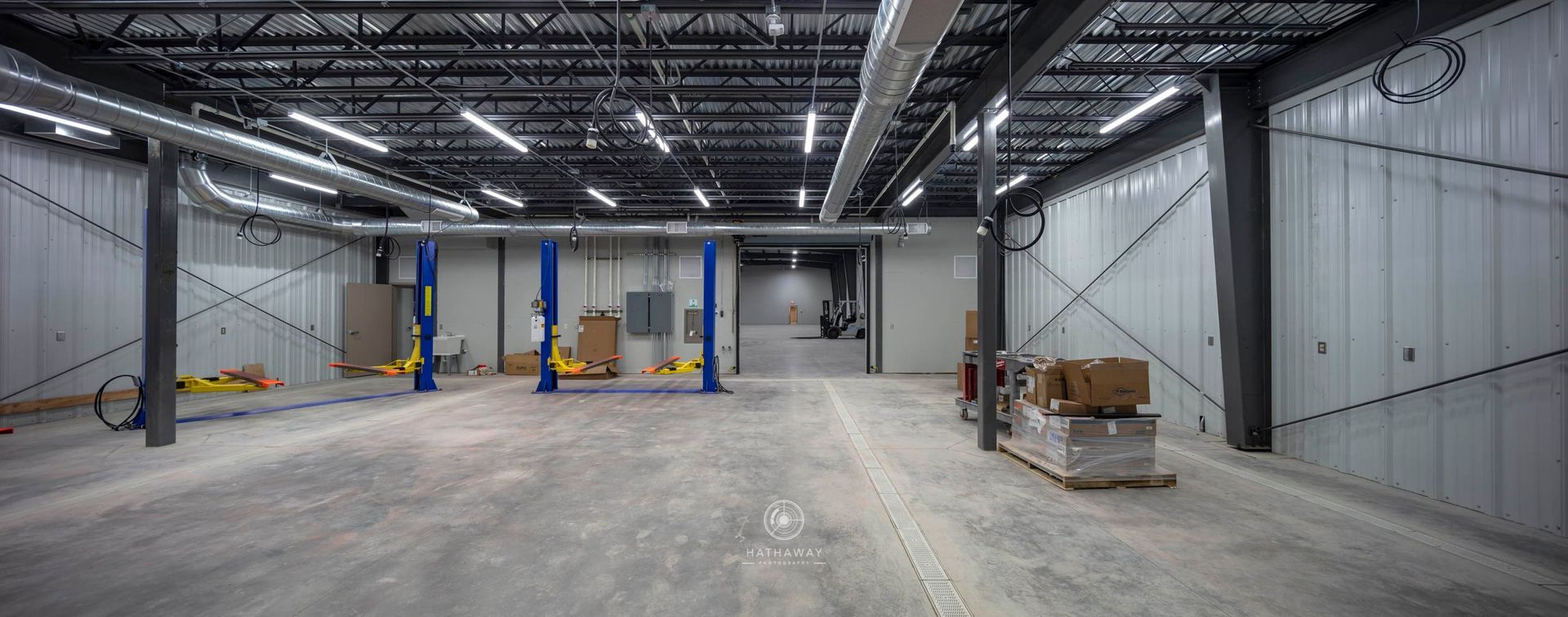 A wide, empty commercial warehouse interior with exposed ceilings, concrete floors, and vehicle service lifts.