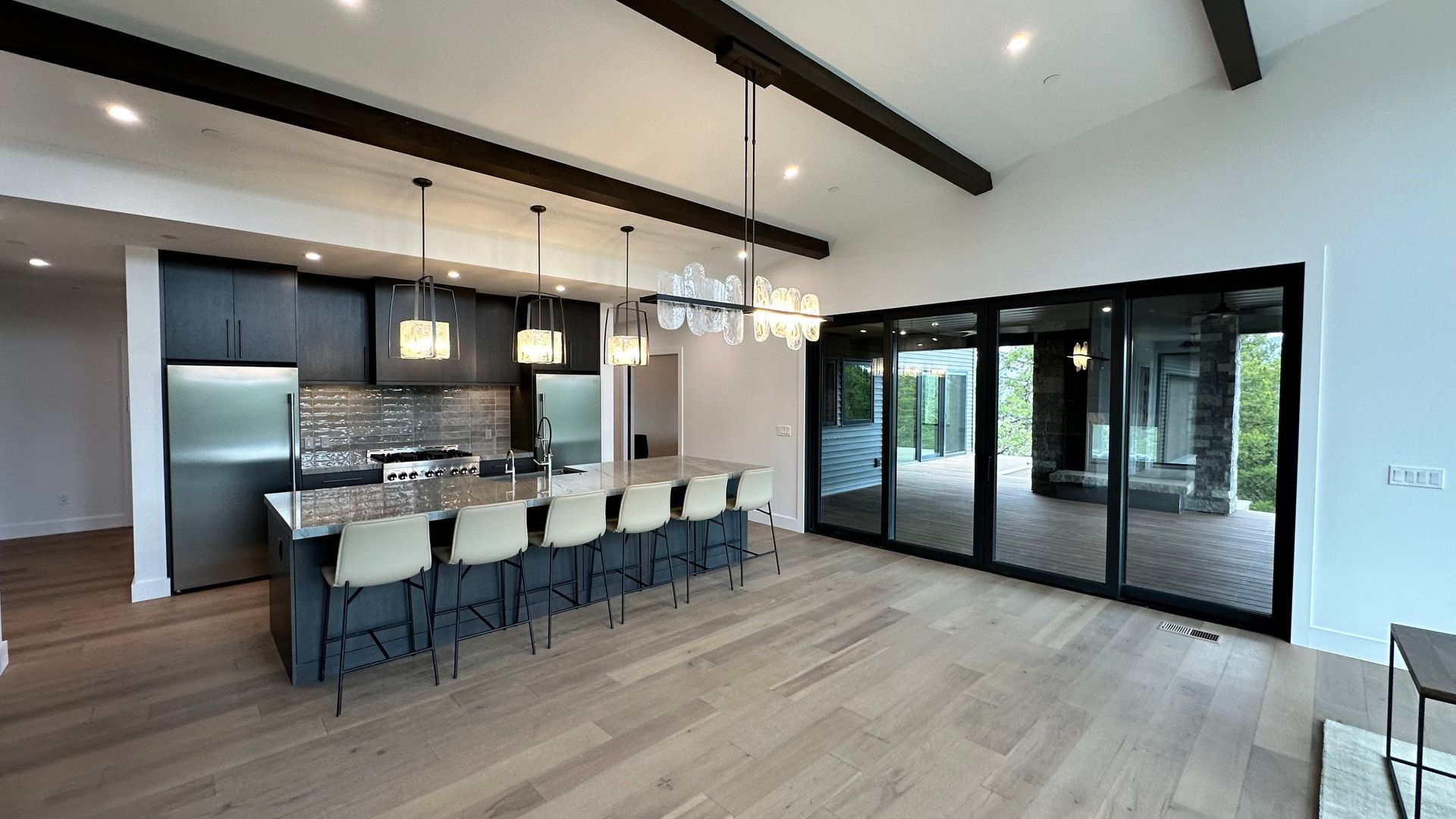Modern kitchen with dark cabinets, a marble-topped island with five stools, hardwood floors, and large sliding glass doors.