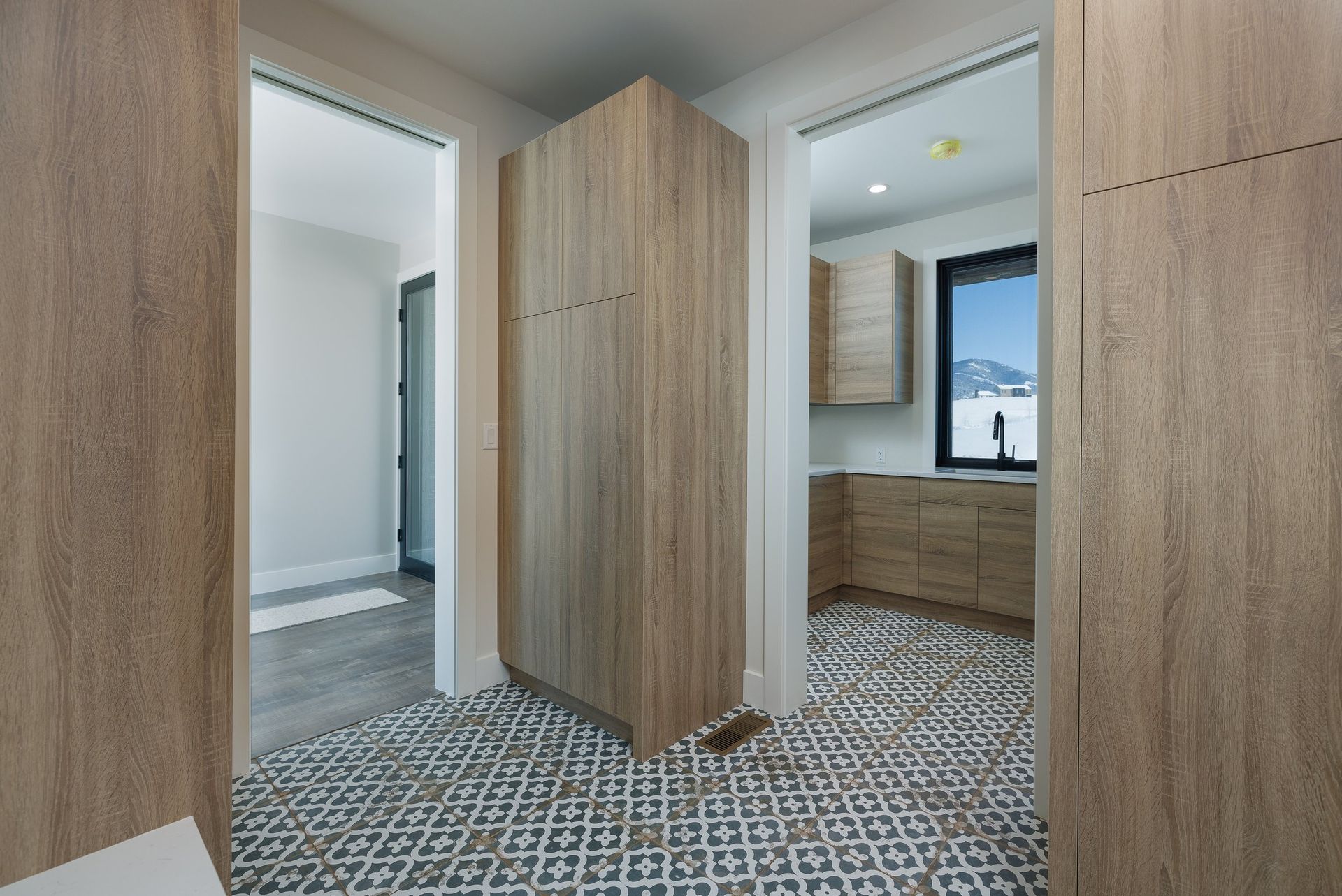 A central wooden cabinet stands in a hall with patterned tile flooring, flanked by two doorways leading to other rooms.