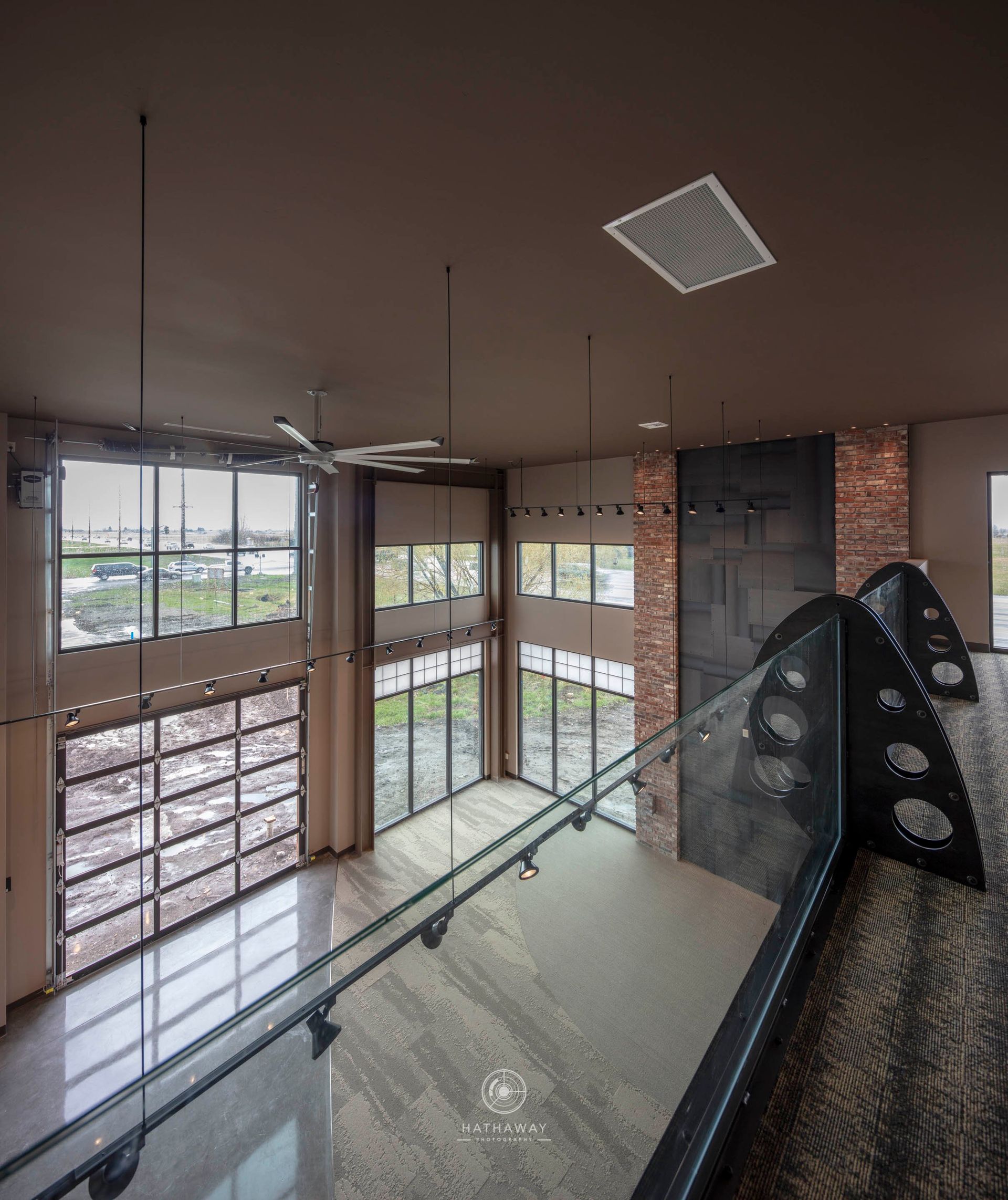 A modern two-story industrial interior with tall windows, brick accents, and a staircase with a unique metal railing.