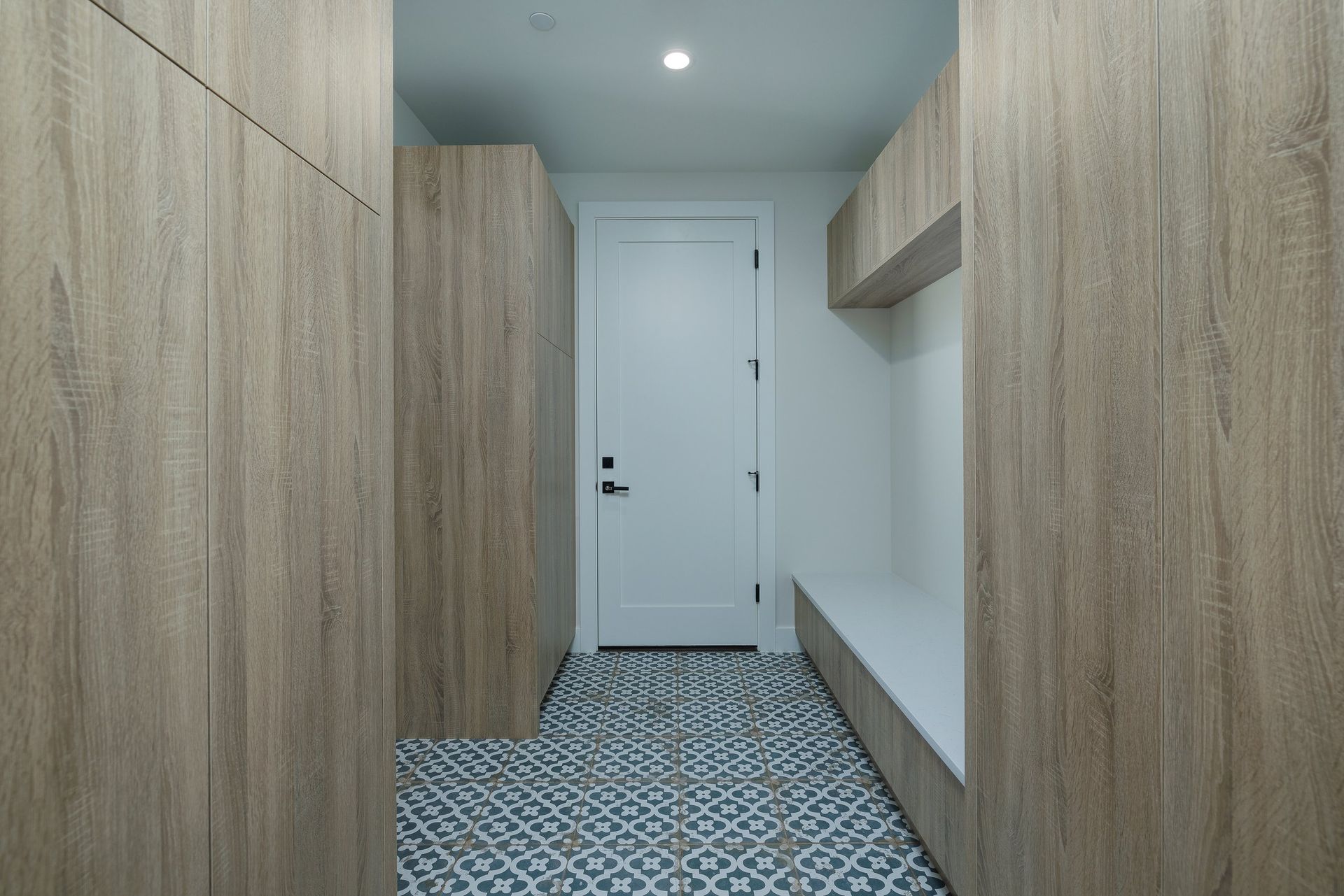 A narrow entryway with wood-toned cabinets, a white door, and patterned tile flooring.