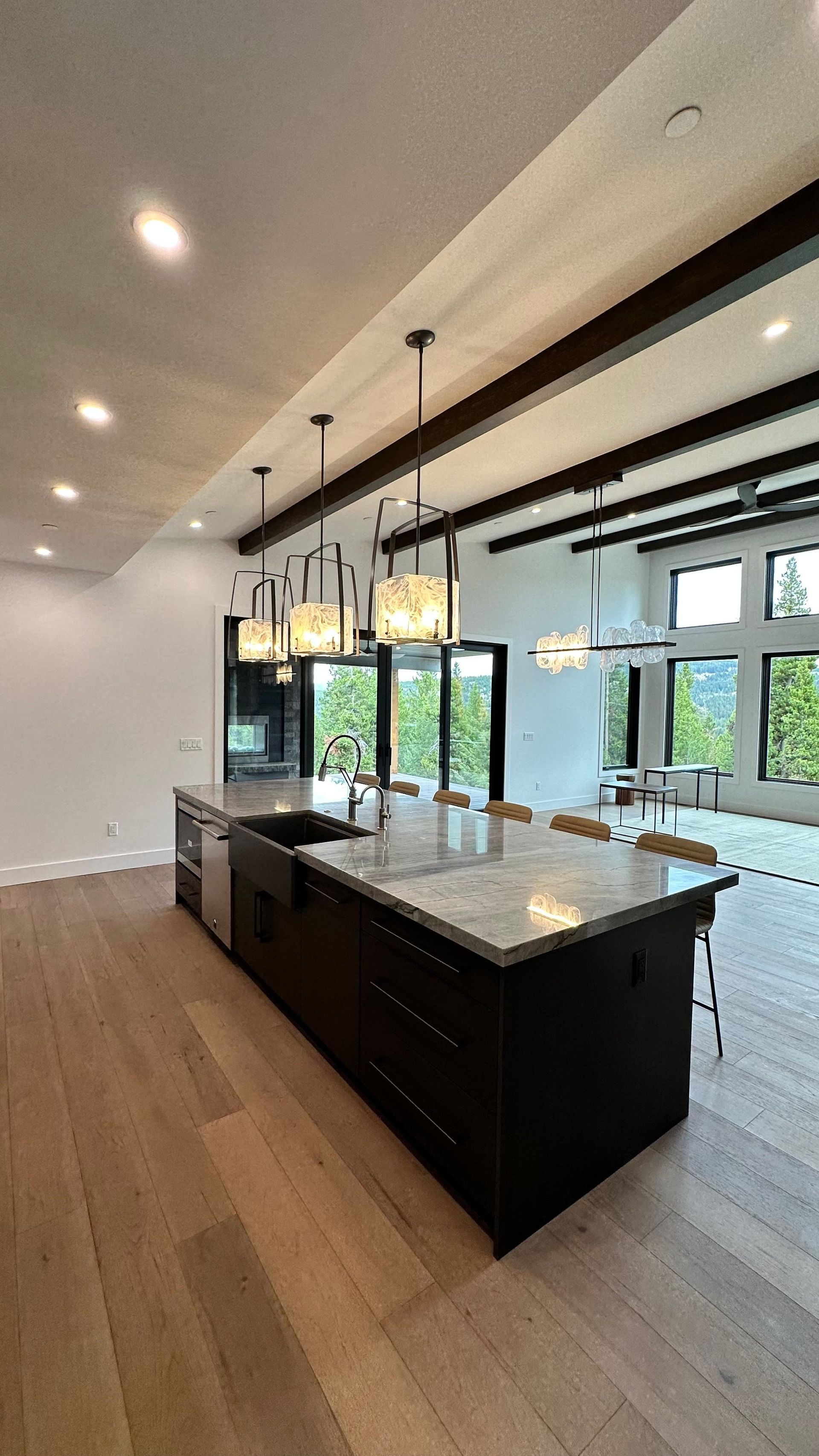 A modern kitchen island with black cabinetry and a light stone countertop, featuring three glass pendant lights above.
