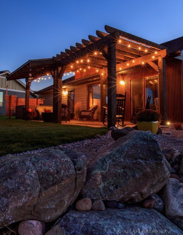 A dimly lit outdoor patio featuring a wooden pergola illuminated by string lights at dusk.