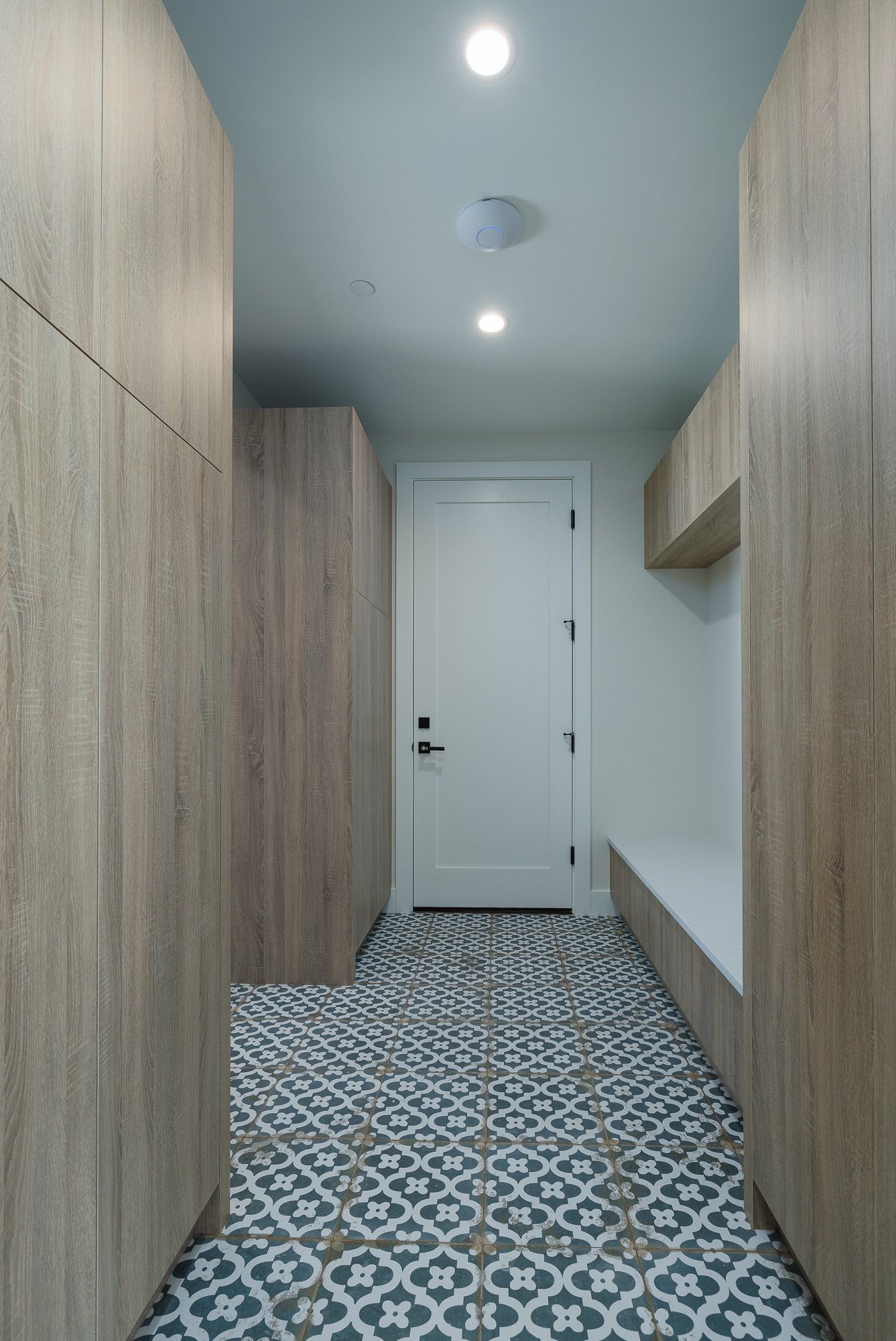 Mudroom entryway with wood cabinets, a white door, and a decorative blue-and-white patterned tile floor.