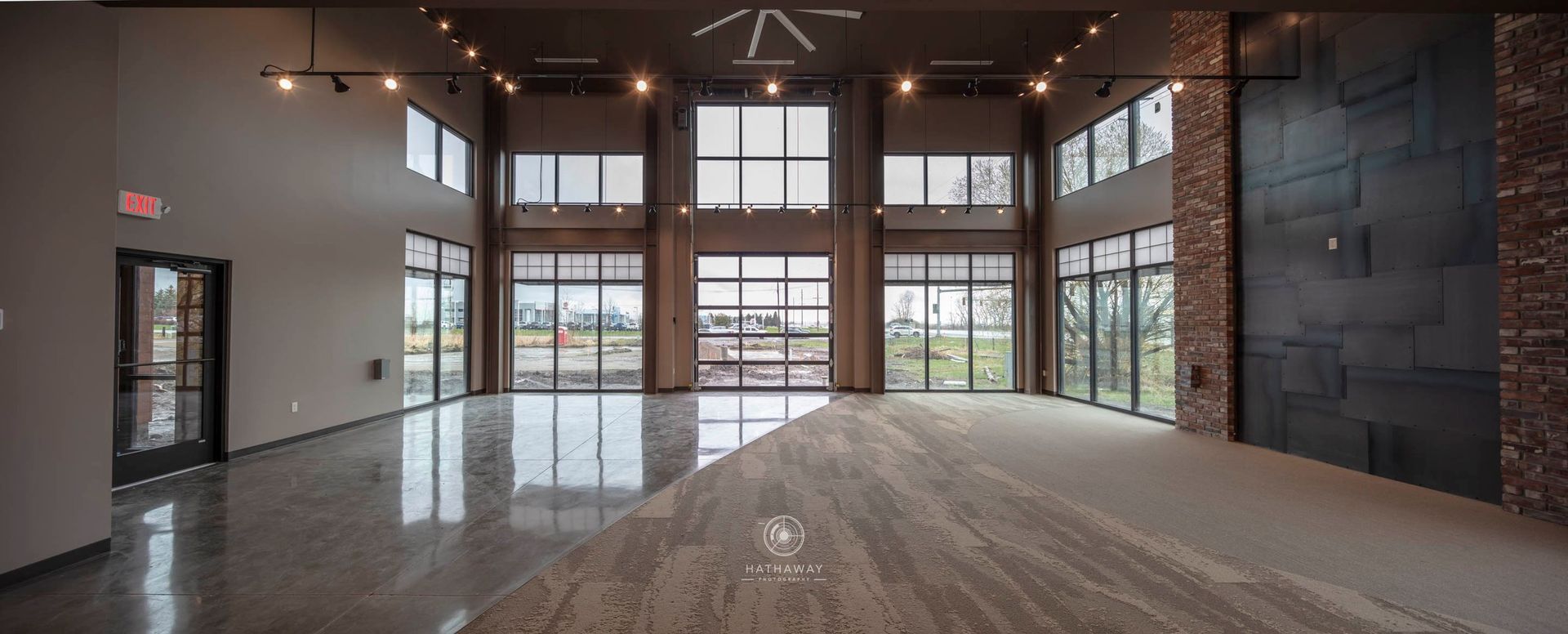 Spacious, modern event hall with tall windows, polished floors, and a dark stone accent wall.