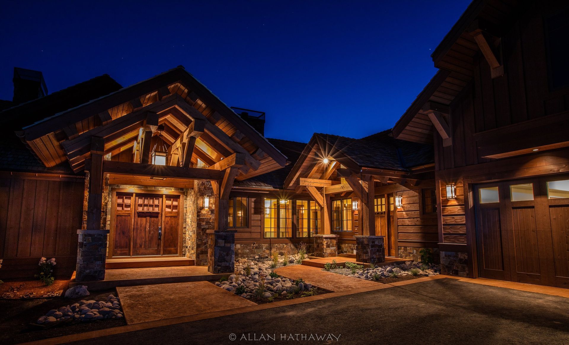 A rustic timber-frame house at night with warm exterior lighting illuminating the entrance and brick walkway.