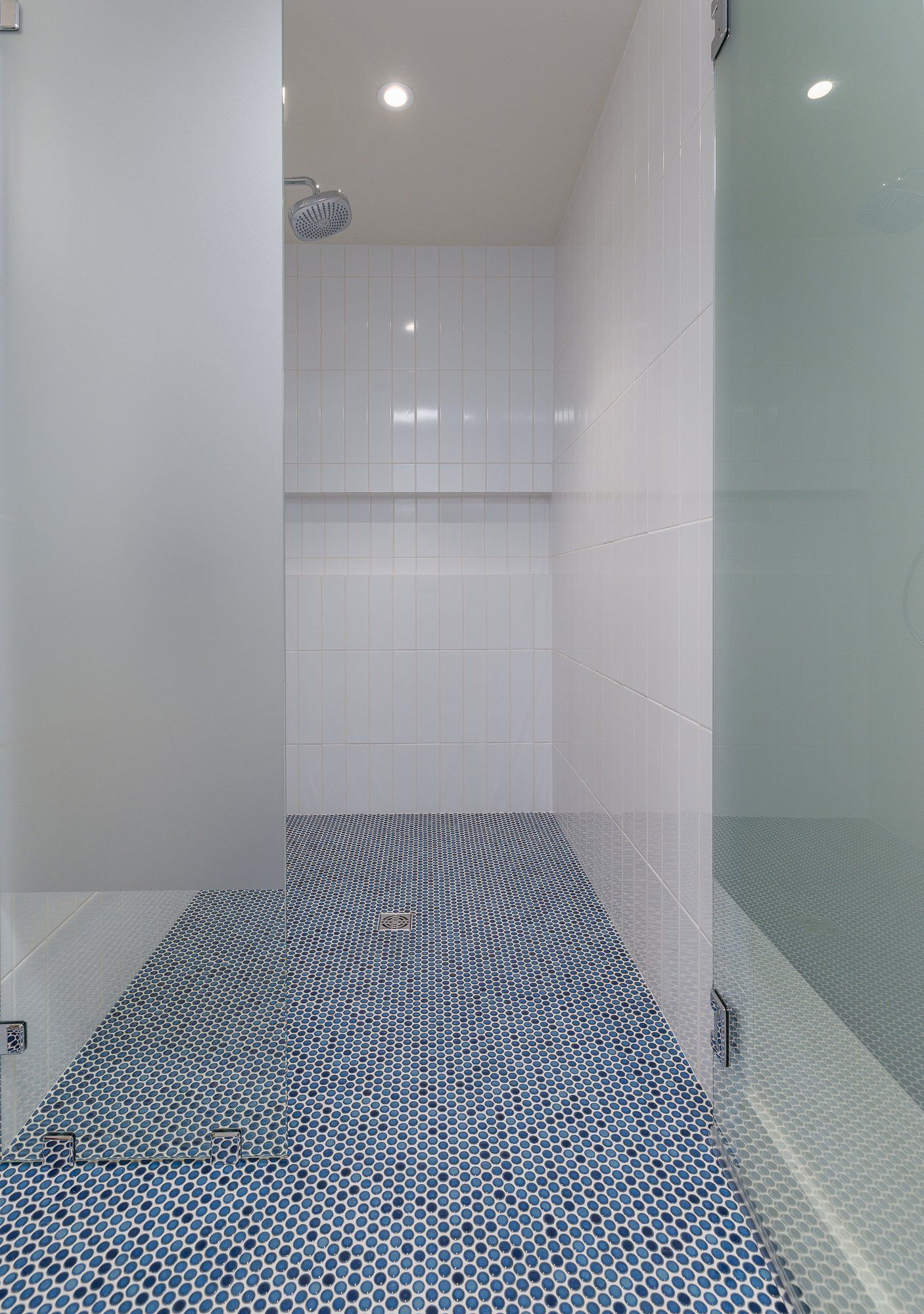 A walk-in shower with white tiled walls, a blue and white patterned tile floor, and a glass partition.