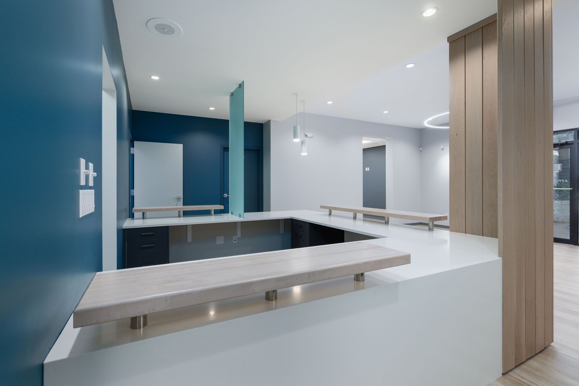 A modern reception desk with a white counter and light wood accents set against dark blue and white walls in an office.