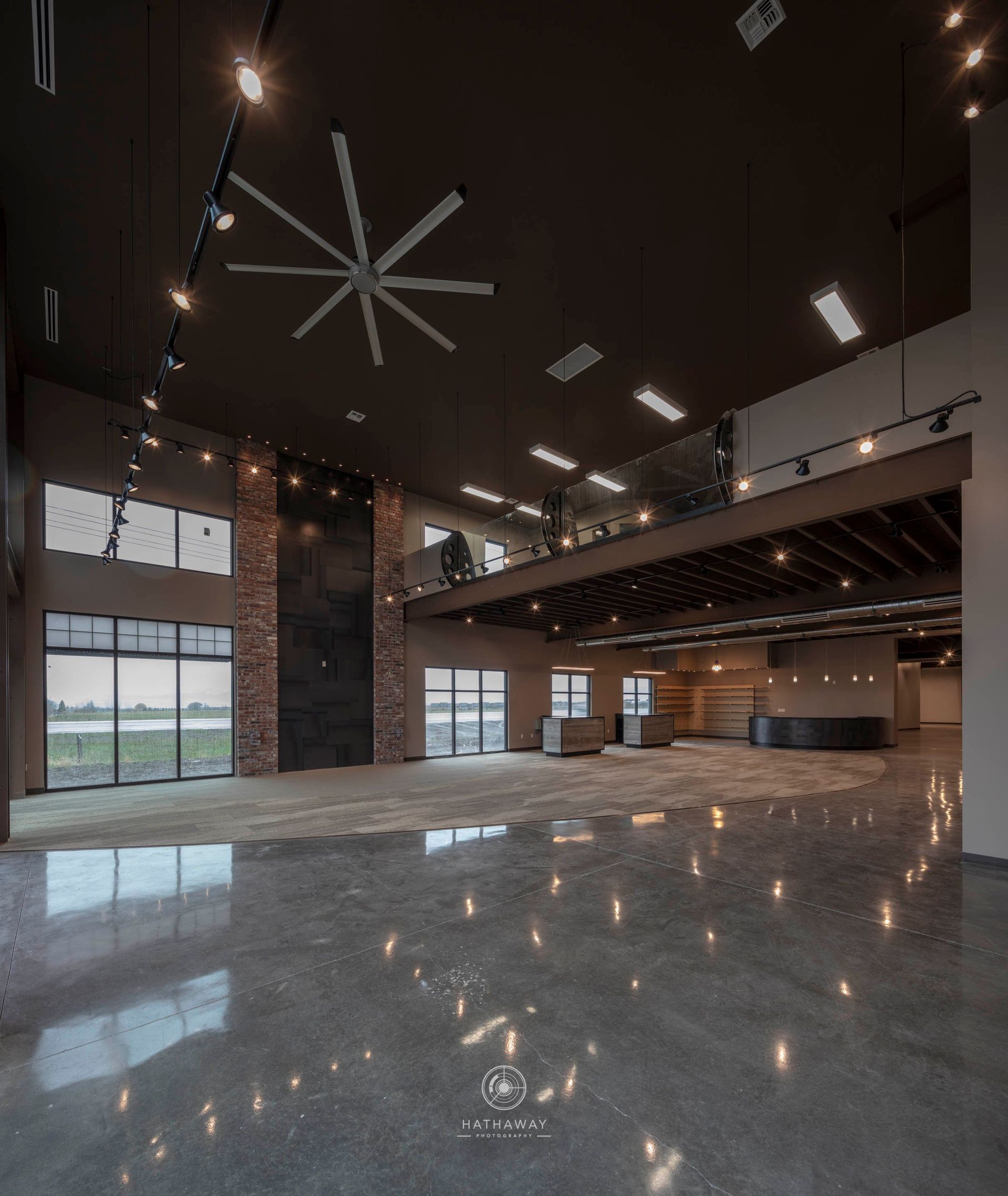 A modern, spacious, open-plan hall with a high dark ceiling, industrial-style lighting, and a polished concrete floor.