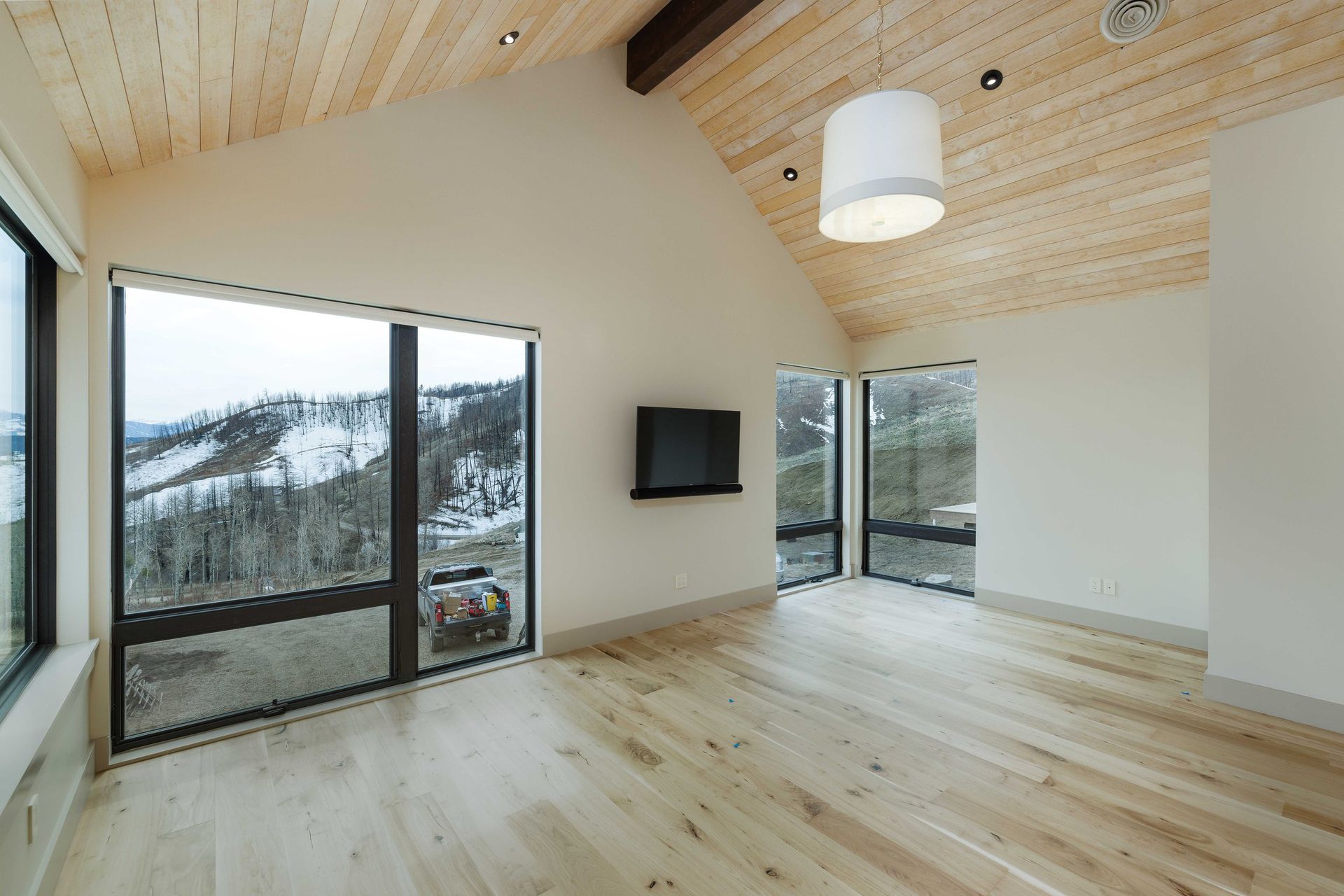 A bright, modern room with light wood floors and vaulted ceilings, featuring large windows with a snowy mountain view.