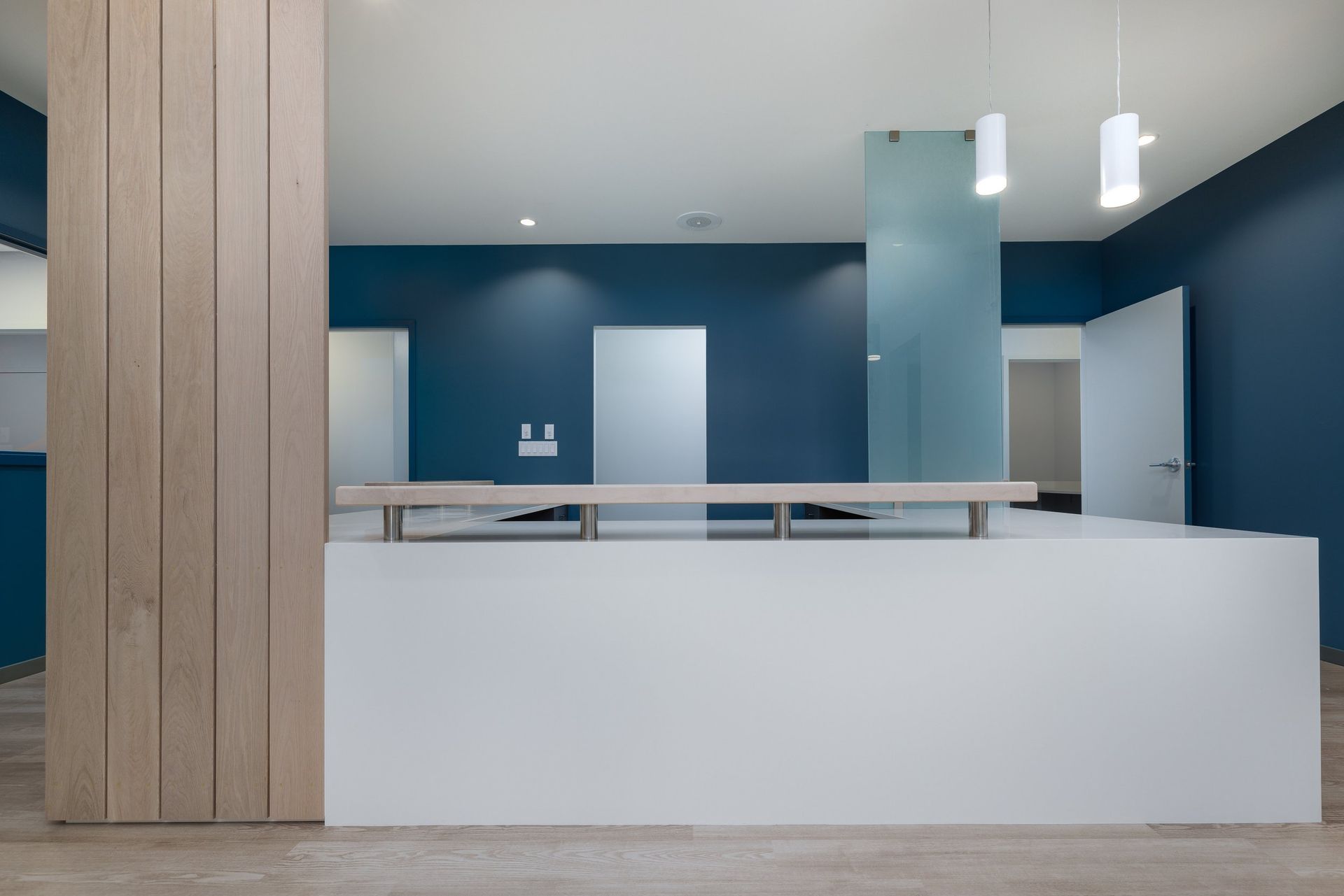 A modern reception desk with a white counter and light wood paneling, set against dark blue walls and a glass partition.