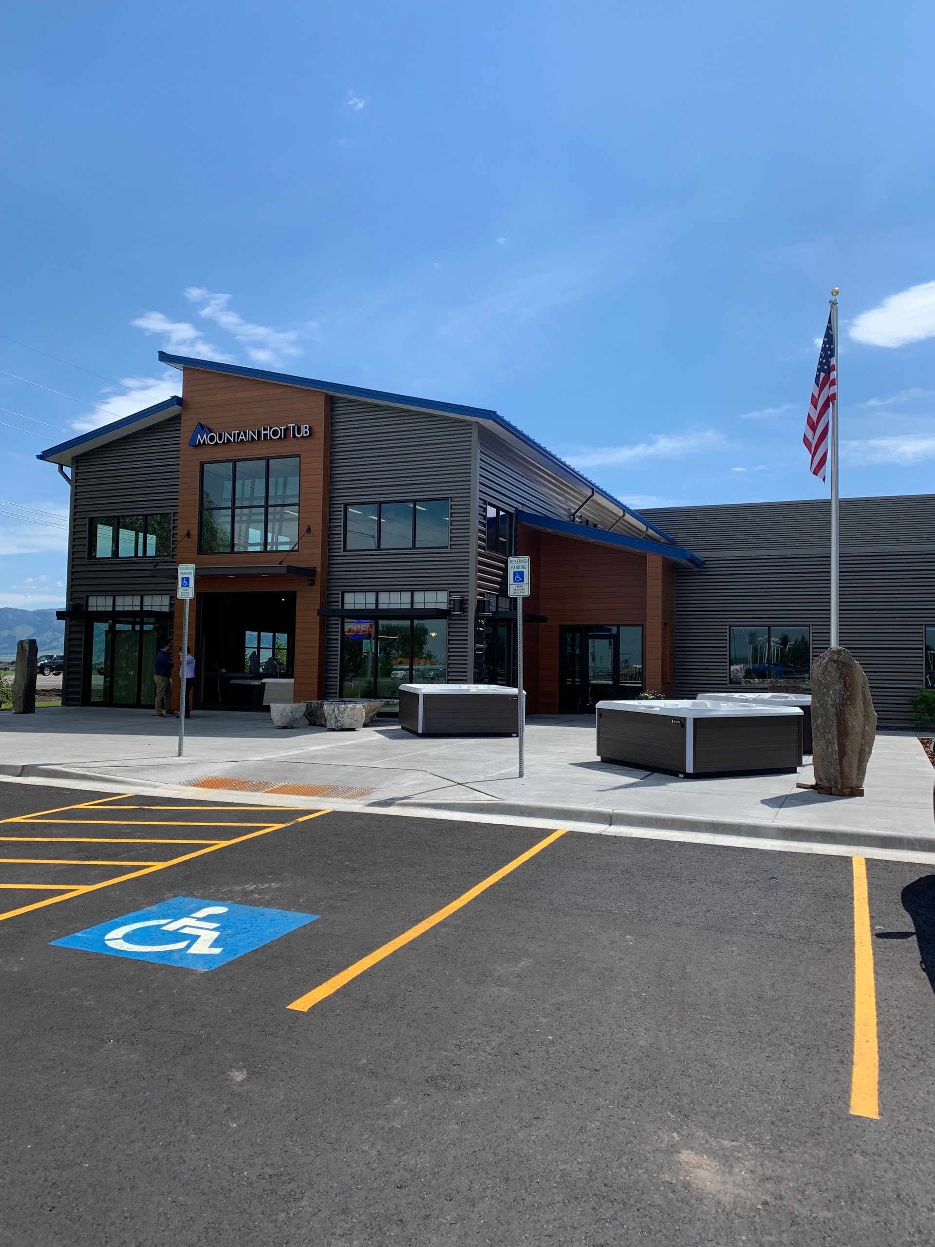 A multi-level building with wood and dark corrugated metal siding, an American flag, and a paved parking lot in front.