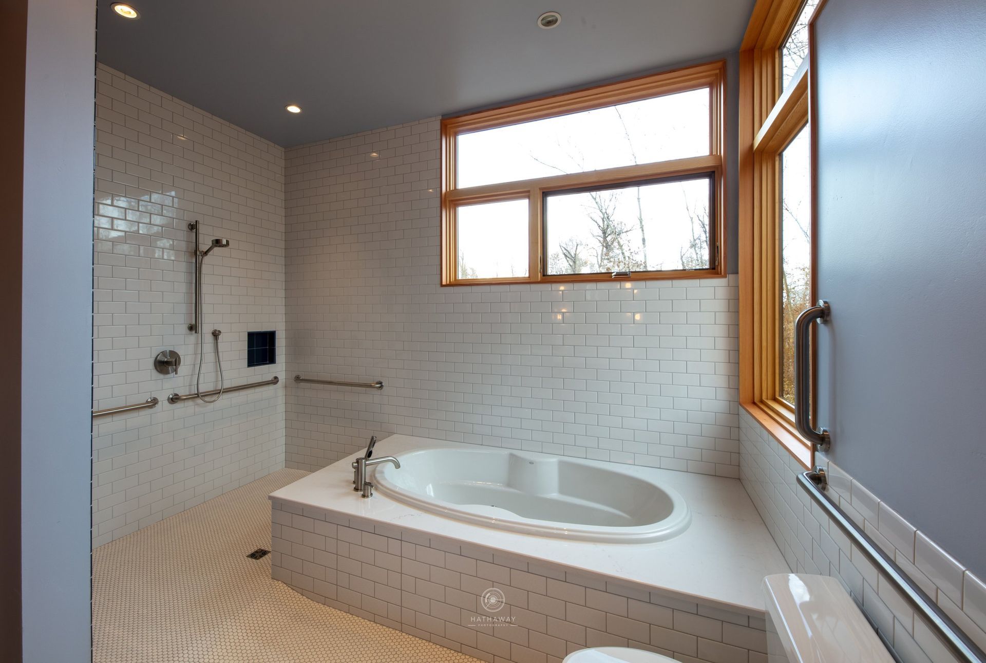 An accessible bathroom with a tiled walk-in shower, a built-in soaking tub, grab bars, and large windows.
