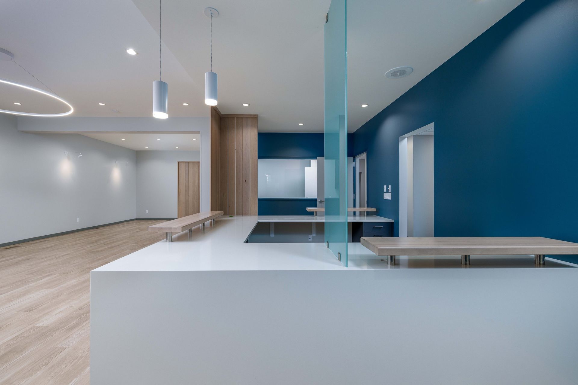 A modern reception area features a white L-shaped desk, a glass partition, and a bold blue accent wall in a bright office.