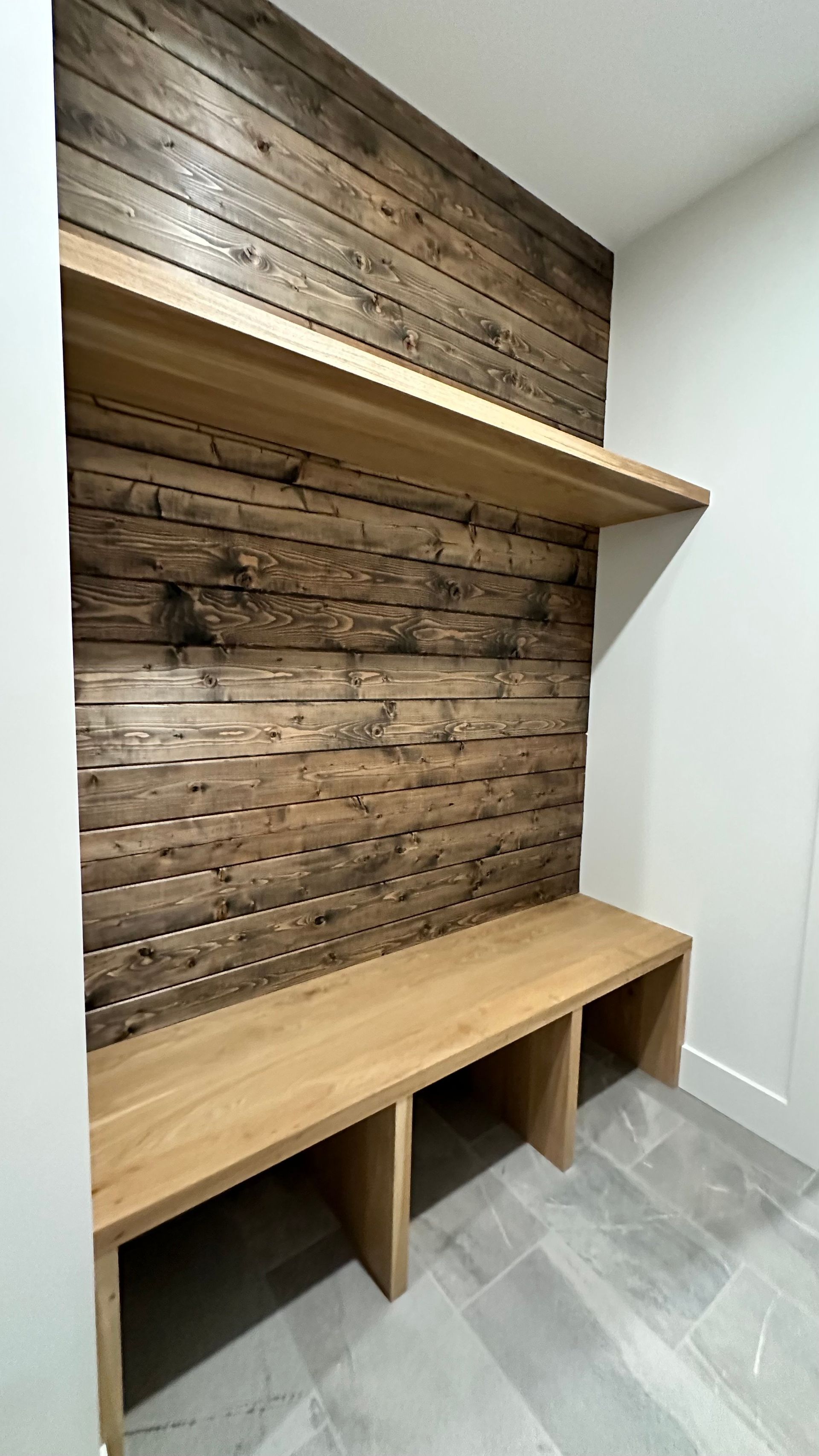 A mudroom bench with light wood seating and a rustic, dark-stained horizontal wood plank wall accent.