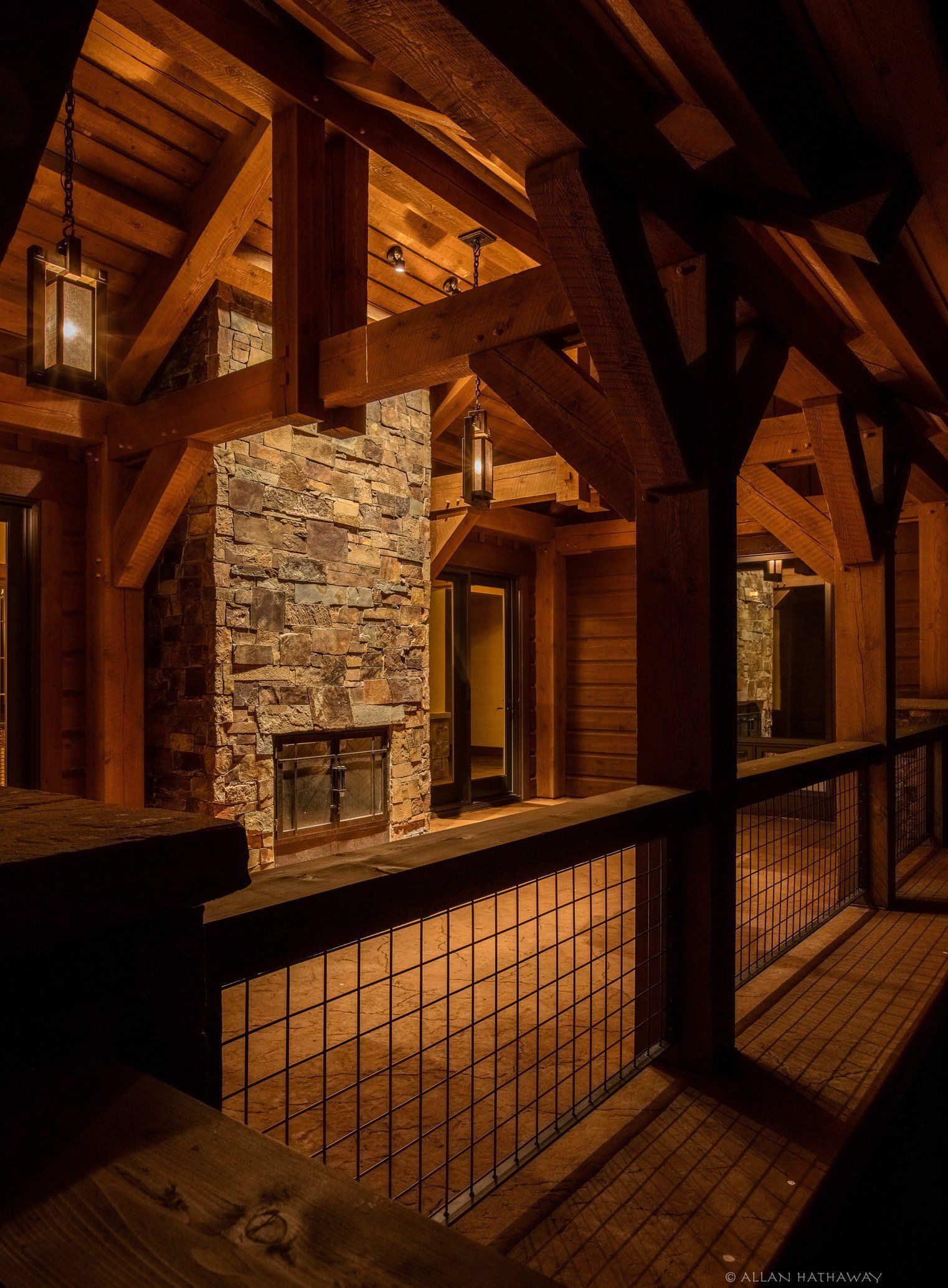 Rustic wooden porch with exposed beams, a stone fireplace, and a metal railing at night.