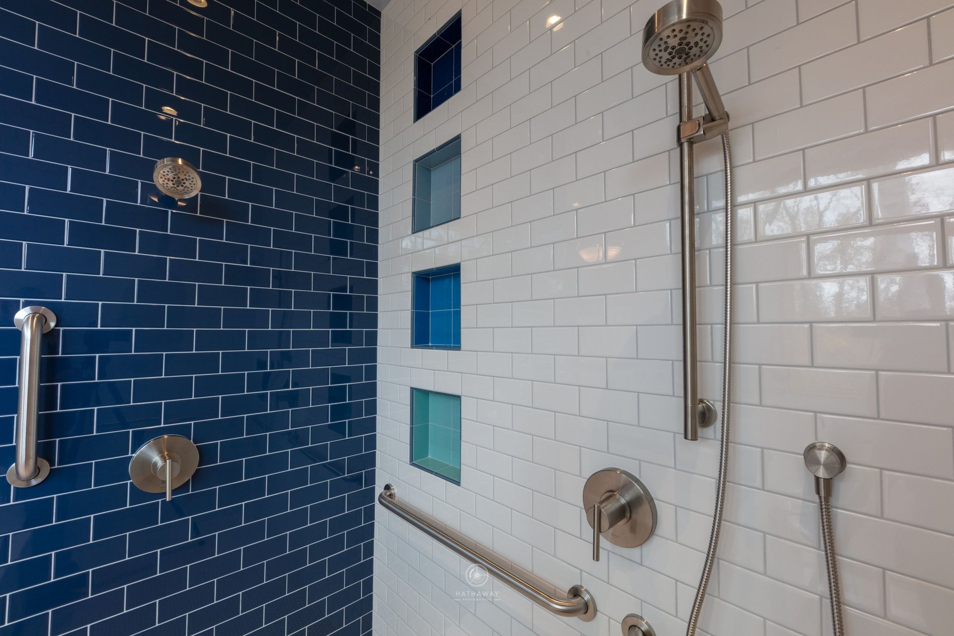 A modern shower with contrasting navy and white subway tiles, a handheld showerhead, grab bars, and recessed wall niches.