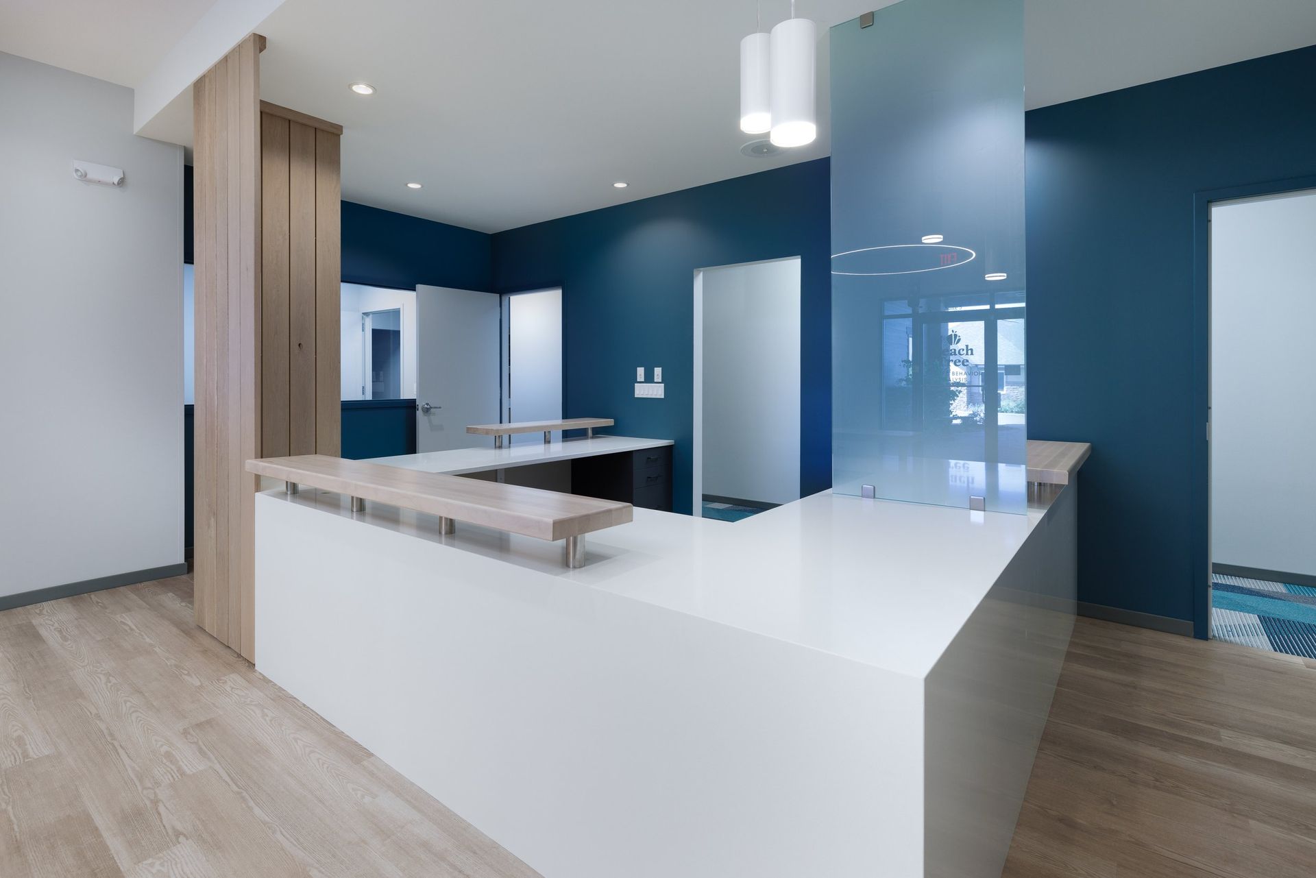 A reception area featuring a white L-shaped desk, wood-grain cabinets, blue accent walls, and a glass partition.