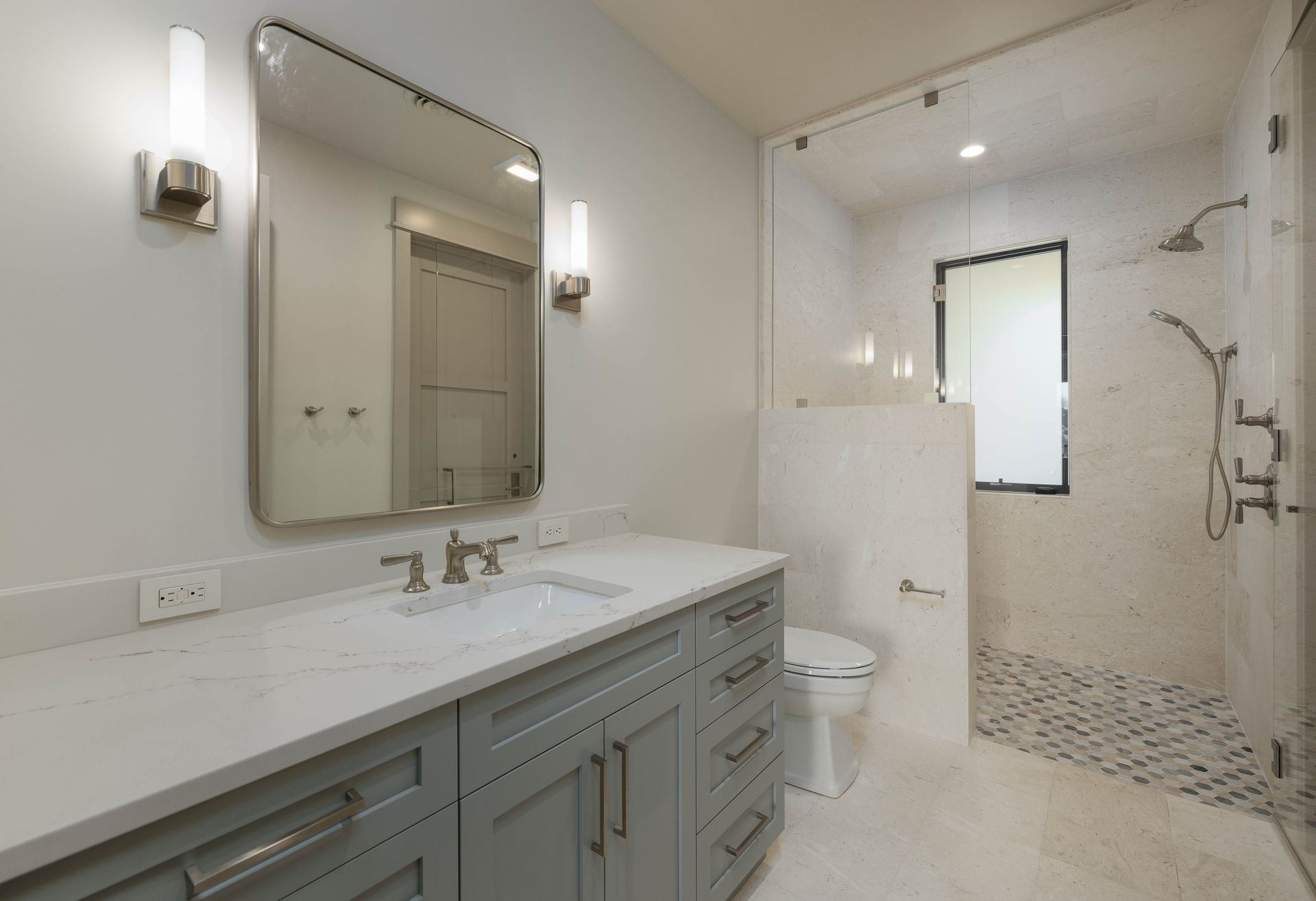 A modern bathroom with a light grey vanity, white quartz countertop, framed mirror, and a walk-in glass shower.