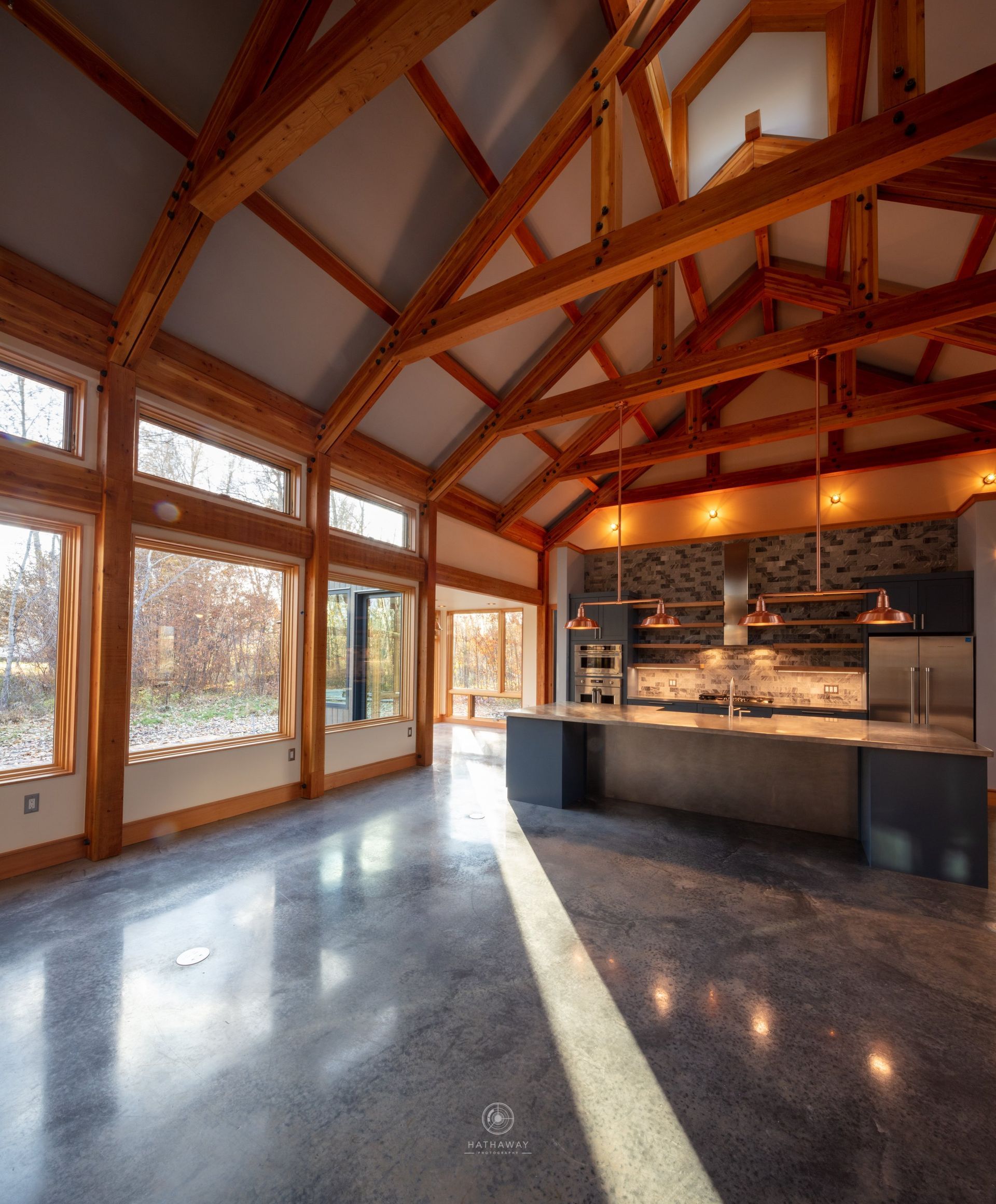 Modern kitchen featuring polished concrete floors, large windows, and a dramatic exposed timber beam ceiling.