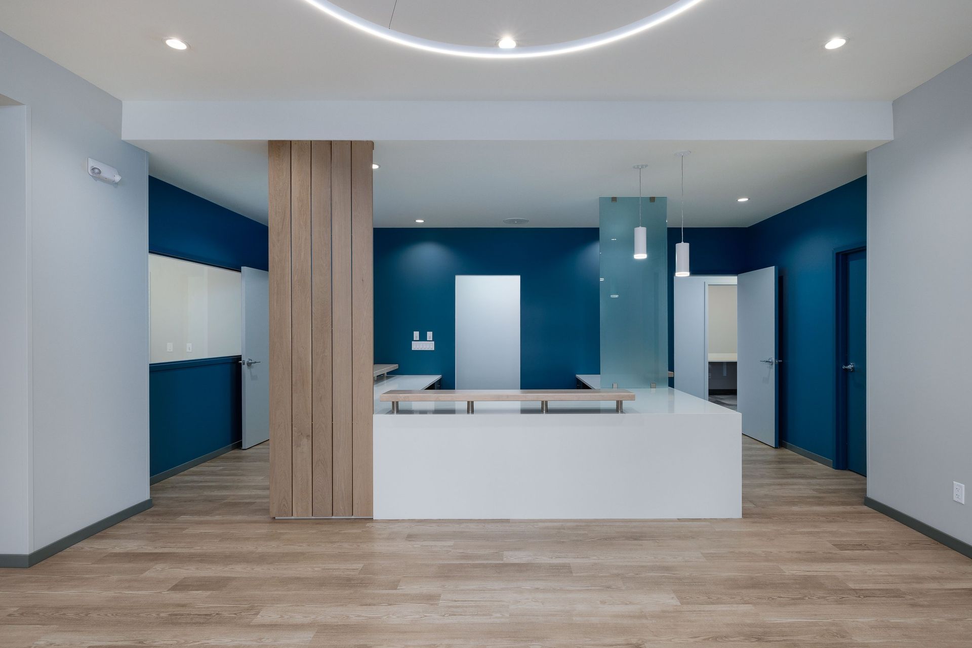 Modern reception area with a white desk, blue accent walls, wood paneling, and wood-look flooring under circular lighting.