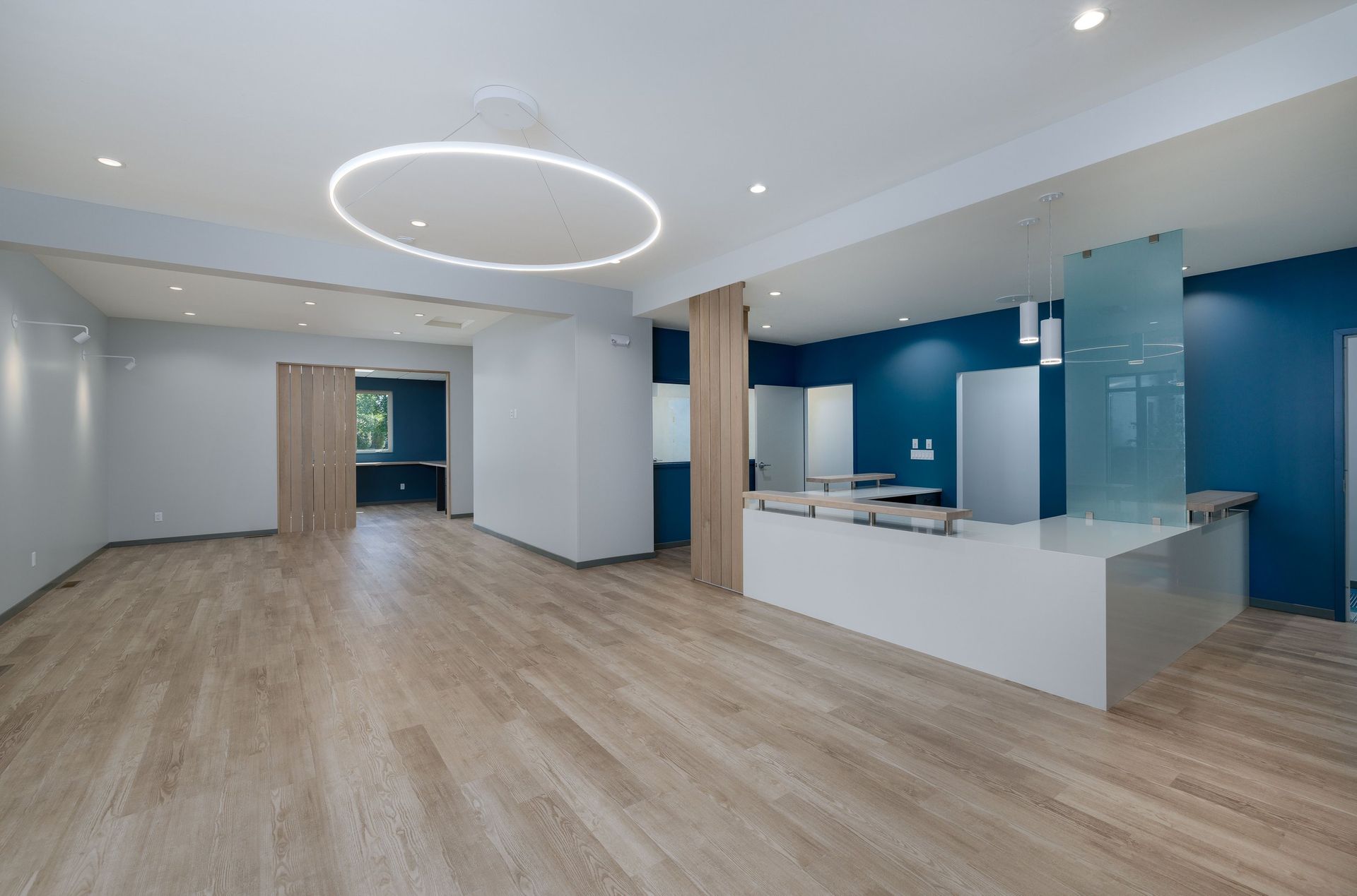 Modern office interior with light wood flooring, white reception desk, and a circular overhead light fixture.