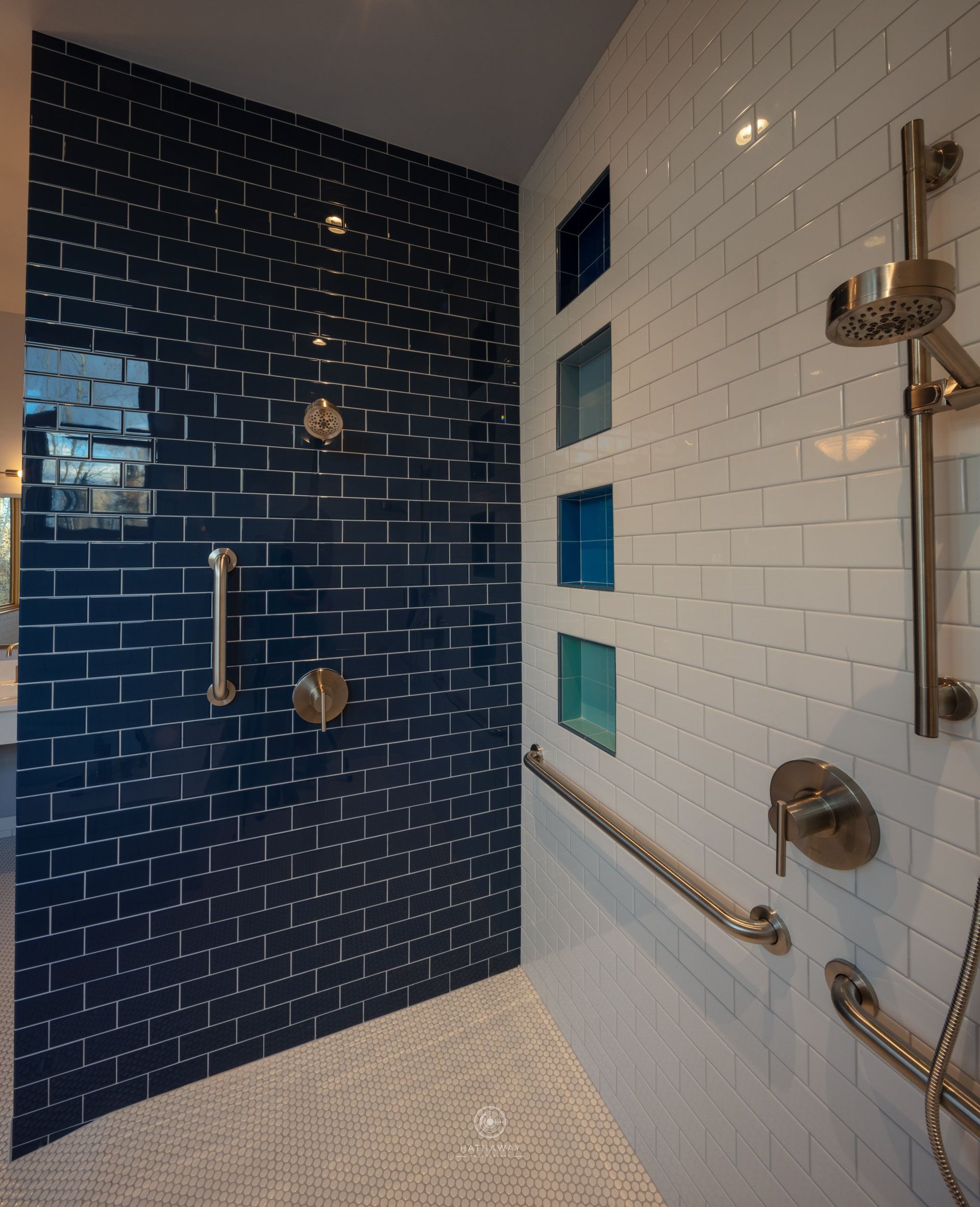 A walk-in shower with blue and white subway tile walls, a hand-held showerhead, and multiple chrome grab bars.