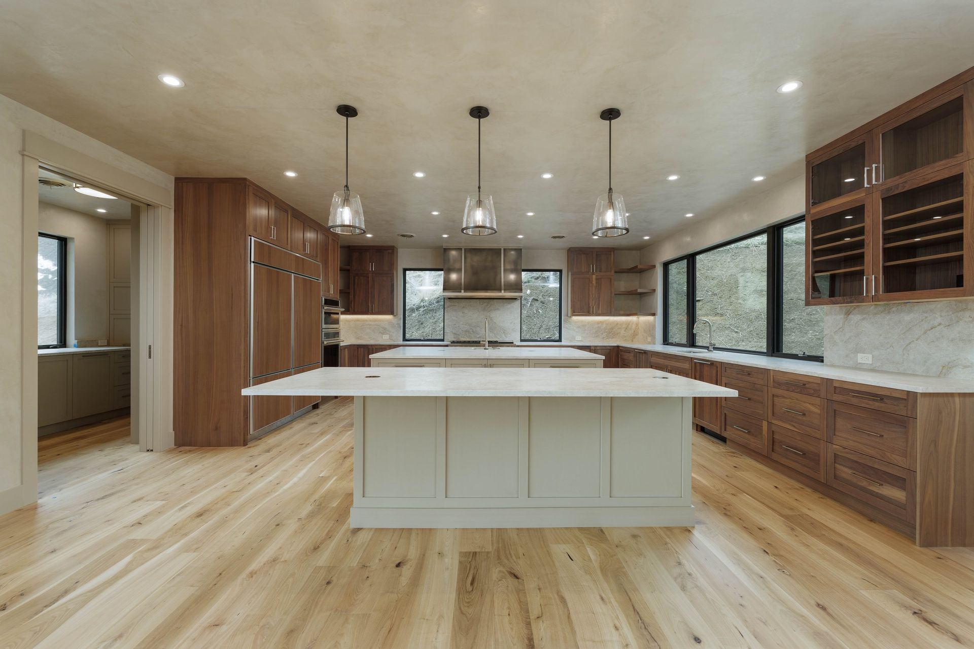 A modern, open-plan kitchen featuring a large light-colored island, wood cabinetry, marble countertops, and hardwood floors.