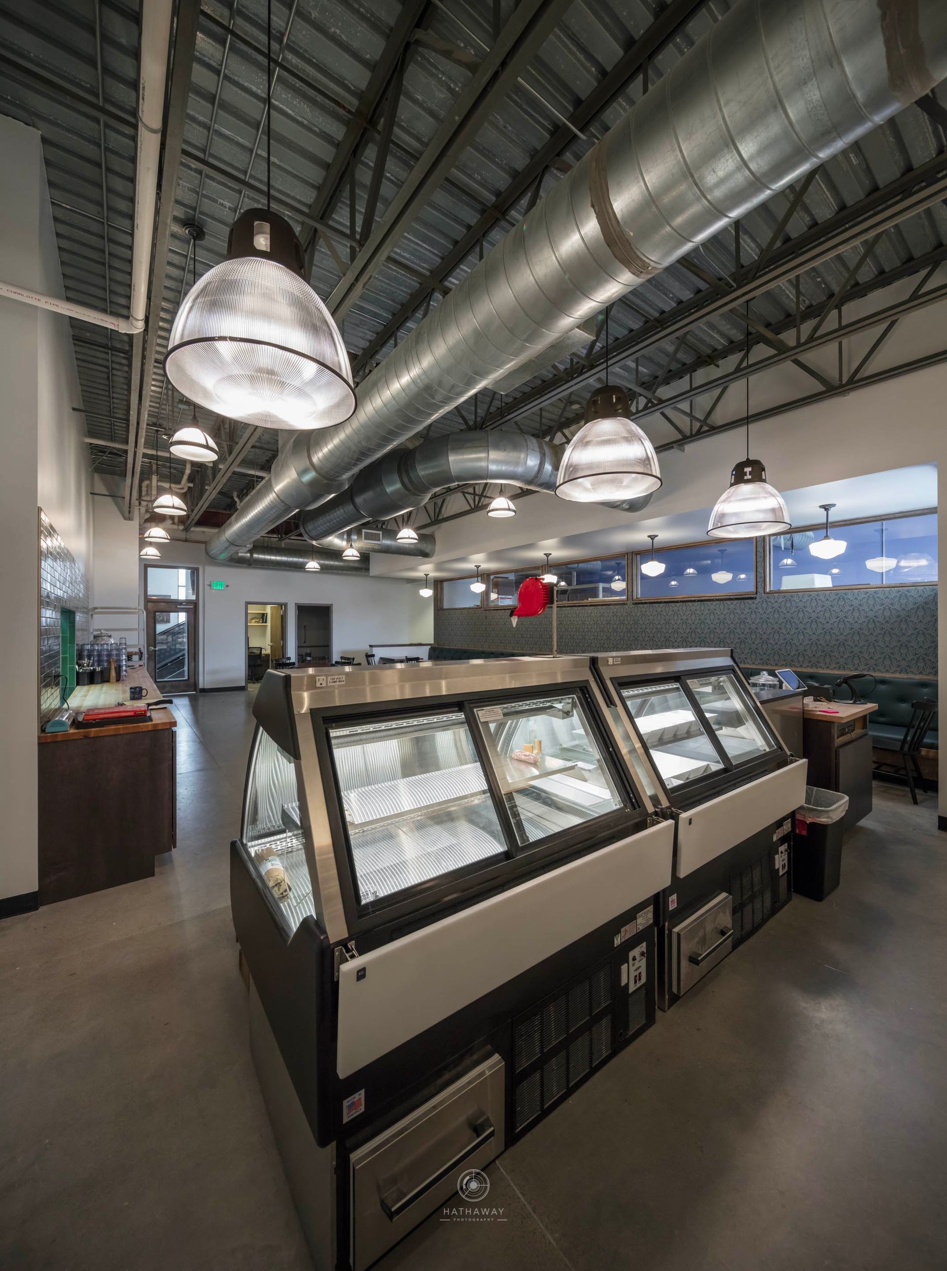 A view inside a modern shop featuring large industrial pendant lights, exposed ductwork, and glass ice cream display cases.