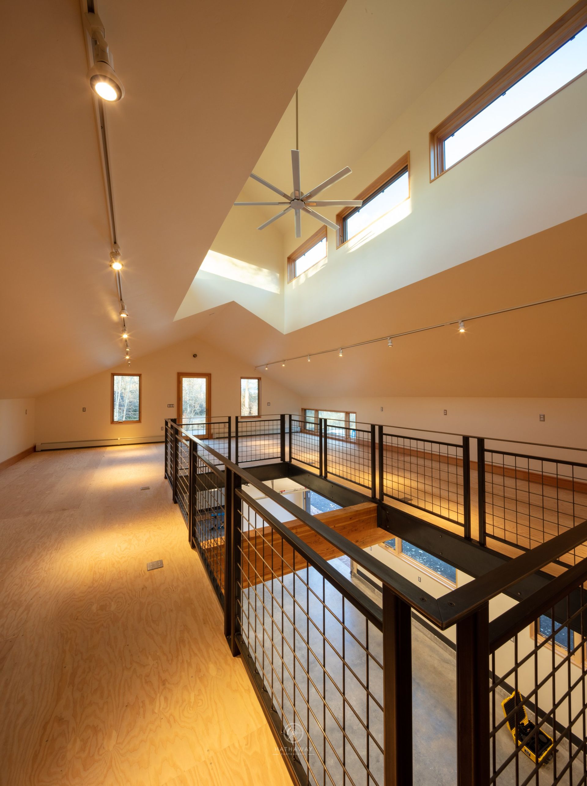 A modern, sunlit interior loft with a metal grid railing overlooking the floor below, featuring high ceilings and skylights.