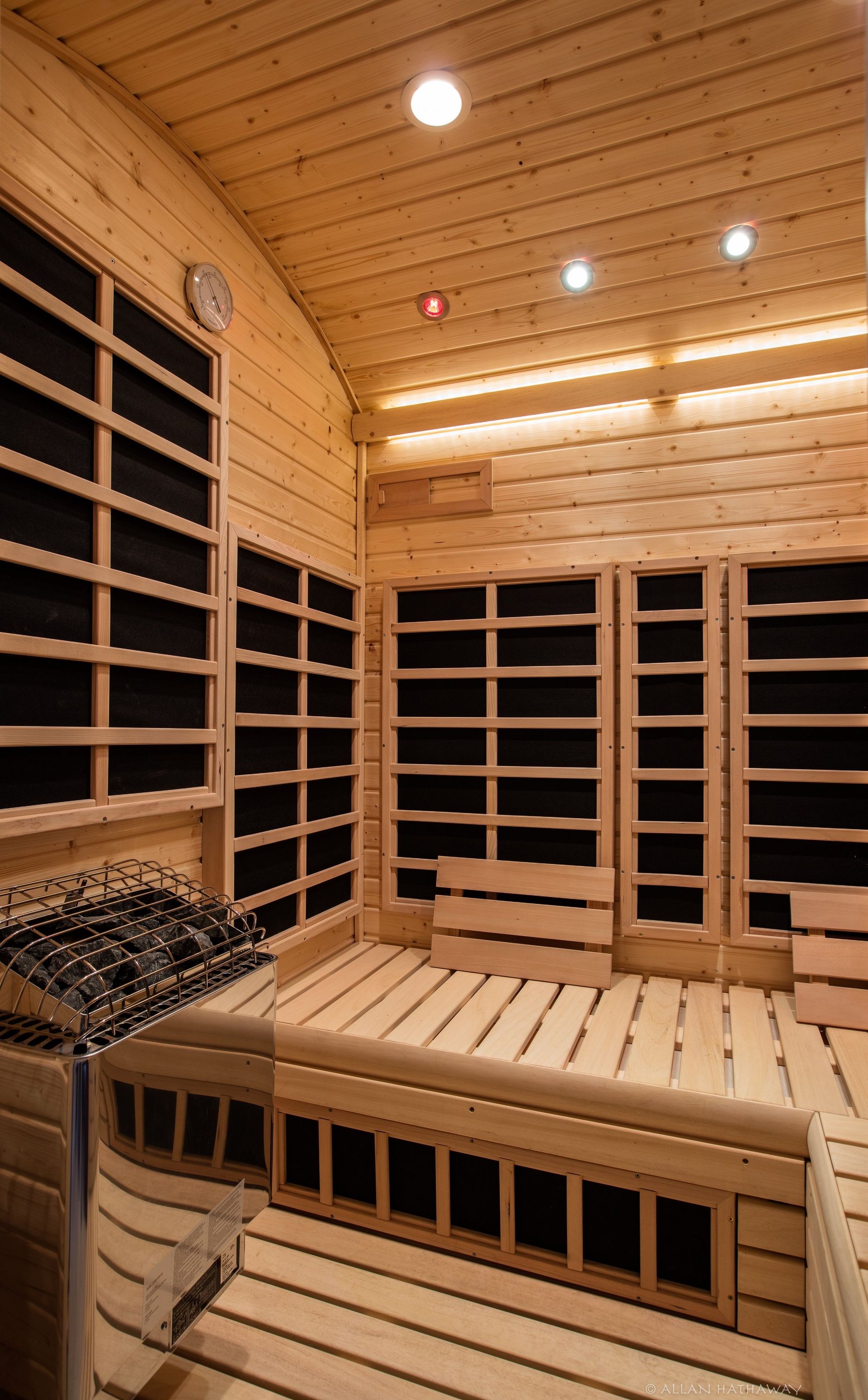 Interior of a wooden sauna featuring slatted benches, backrests, and wall-mounted infrared heating panels.