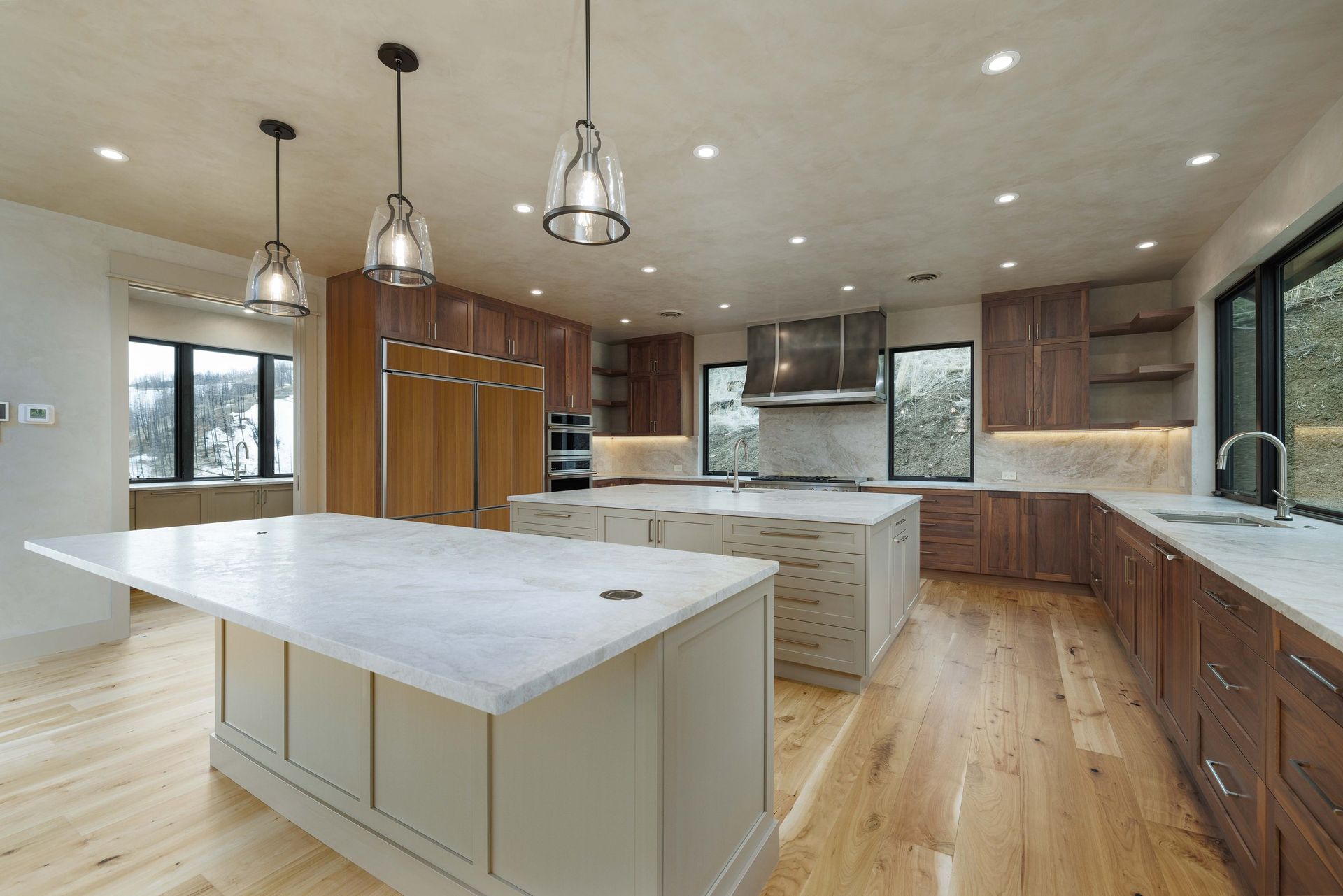 Modern kitchen with two islands, light marble countertops, wooden cabinetry, and pendant lights.