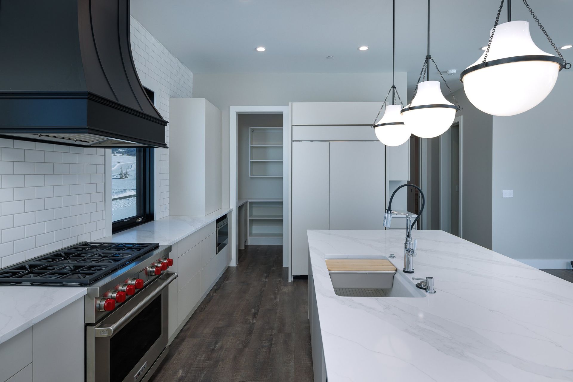 Modern kitchen with a white marble island, stainless steel range, black vent hood, and pendant lights over the sink.