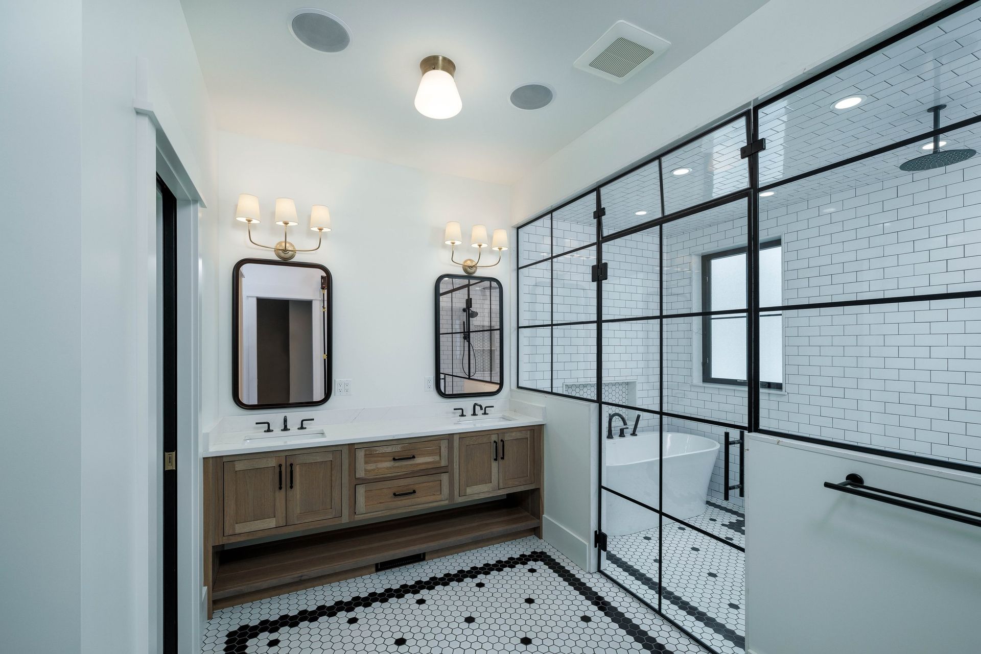 Modern bathroom with a wood vanity, black framed mirrors, and a glass-enclosed shower area with tiled floors.