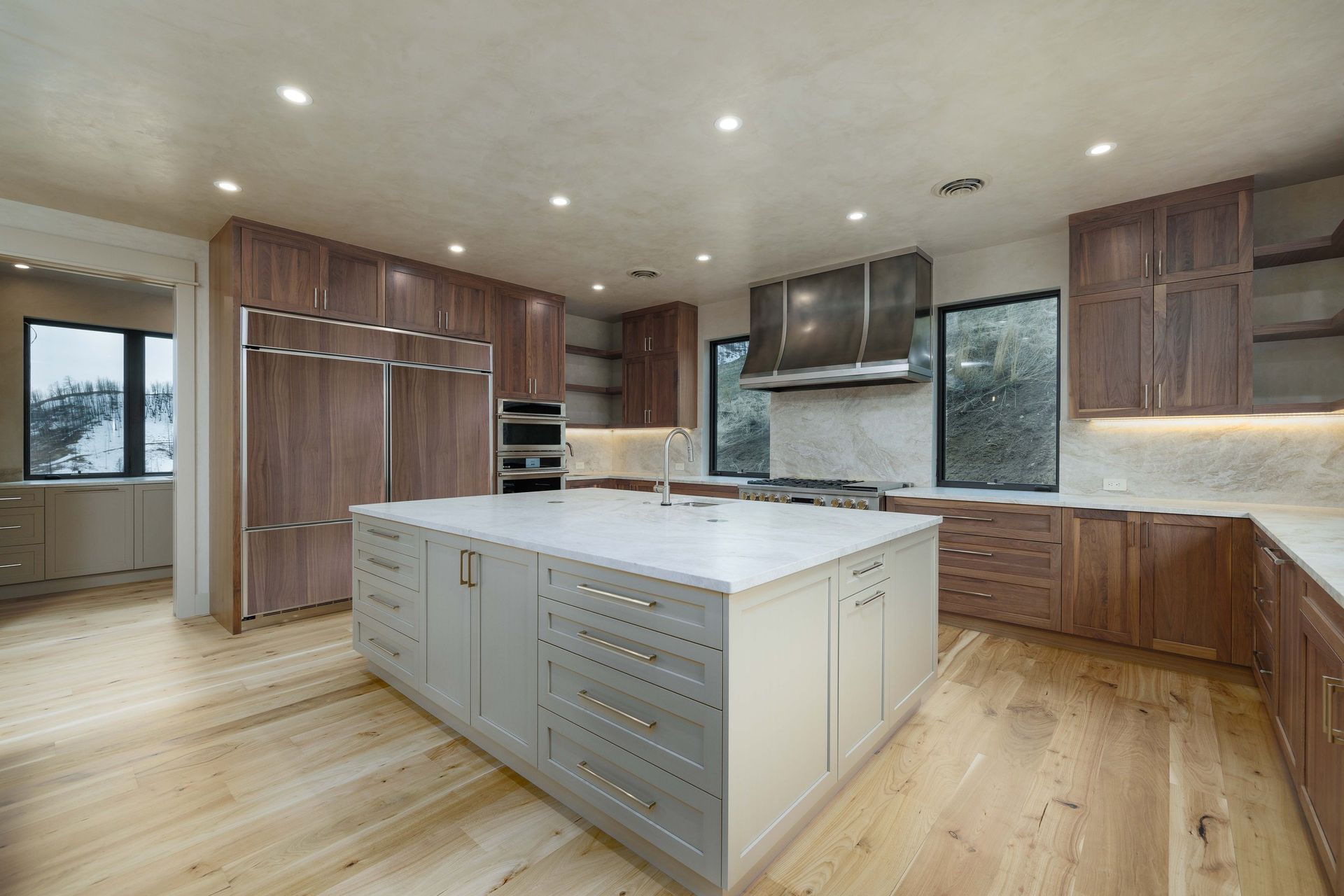A modern kitchen featuring walnut cabinetry, a large grey island with white countertop, and light wood flooring.