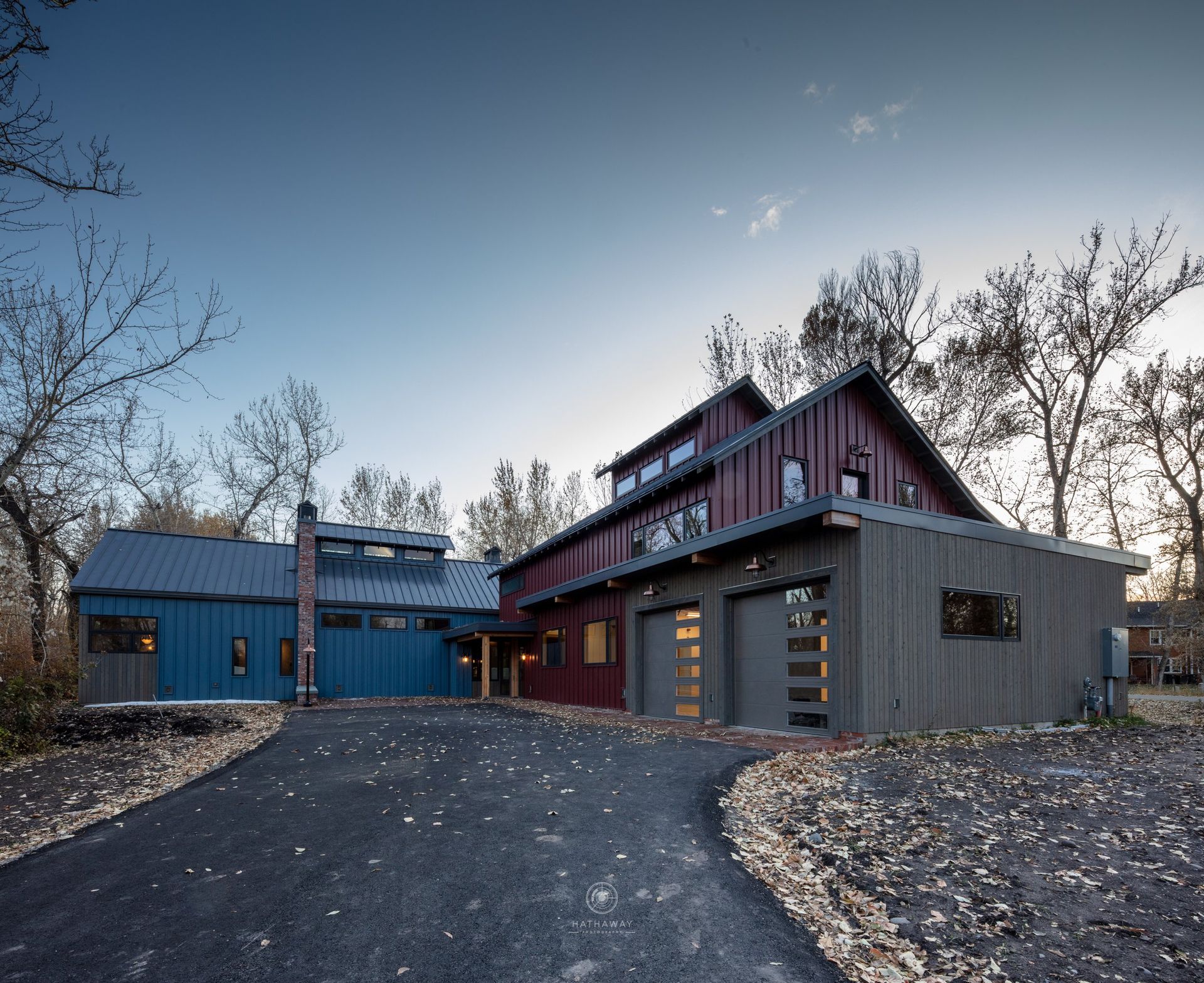 A multi-story modern home with blue and maroon vertical siding and a gray garage, set against trees under a blue sky.