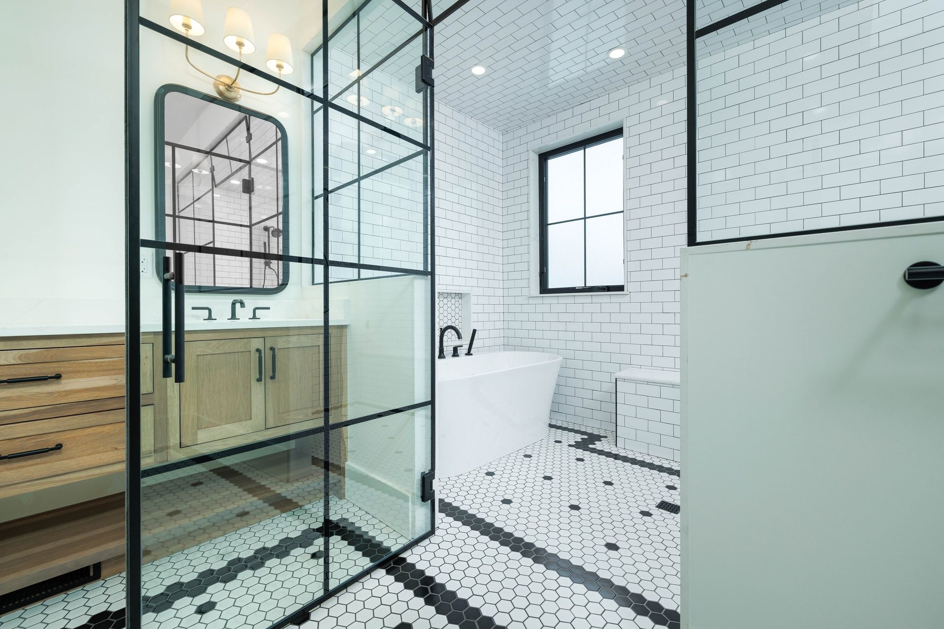 Modern bathroom with a wooden vanity, a freestanding white tub, and black and white patterned tile flooring.